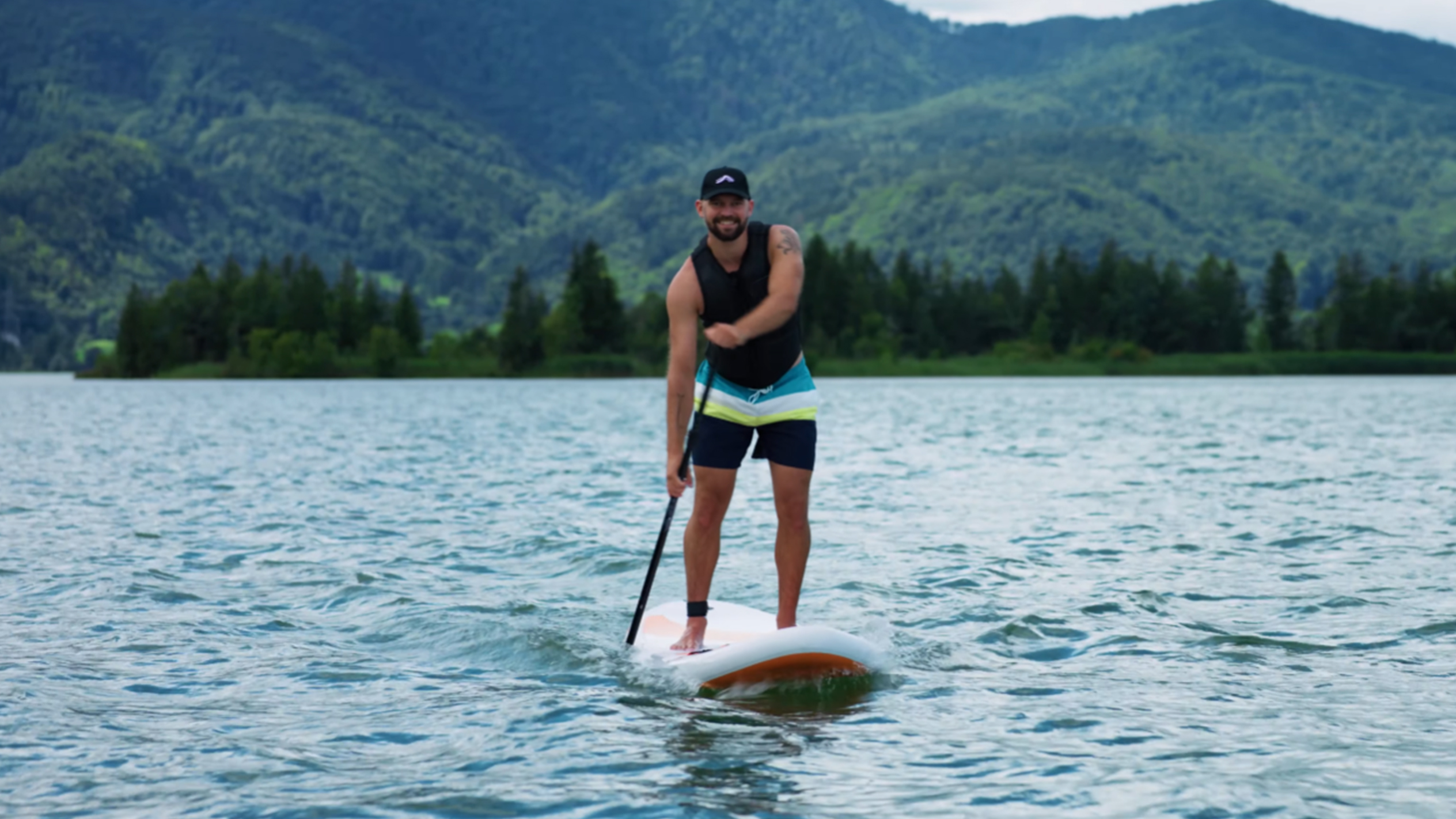 Man op paddleboard op een meer met bergen op de achtergrond.