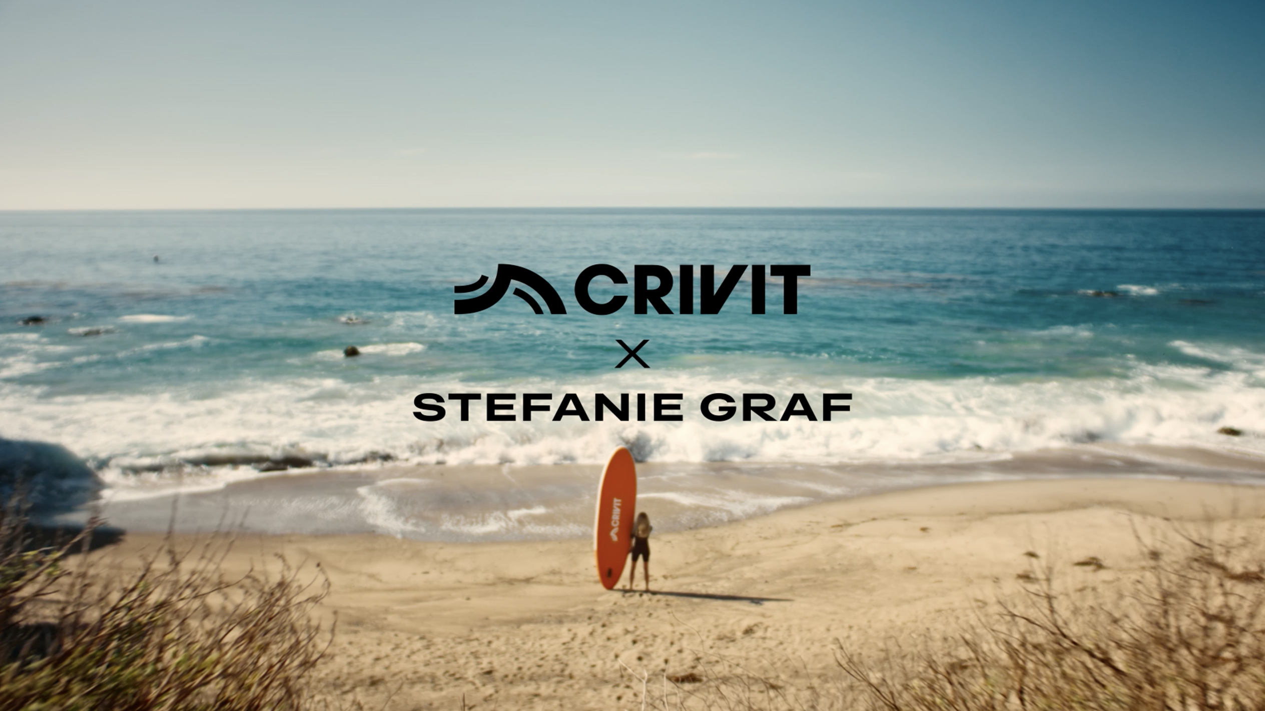 Vrouw met een oranje SUP-board op een zandstrand, met de zee op de achtergrond.