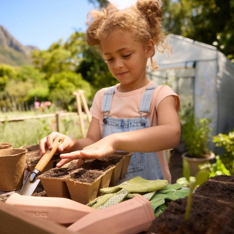 Meisje plant zaden in kweekpotjes met tuingereedschap en handschoenen.