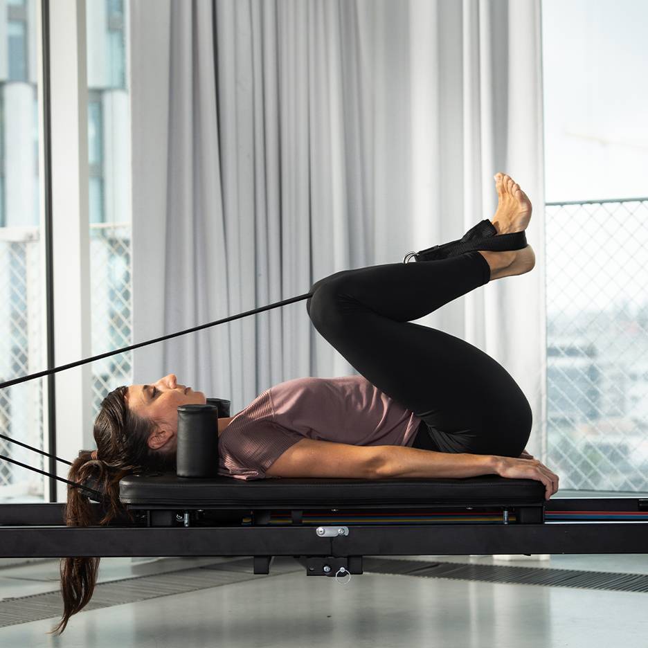 Vrouw doet Pilates op een reformer met de benen omhoog.