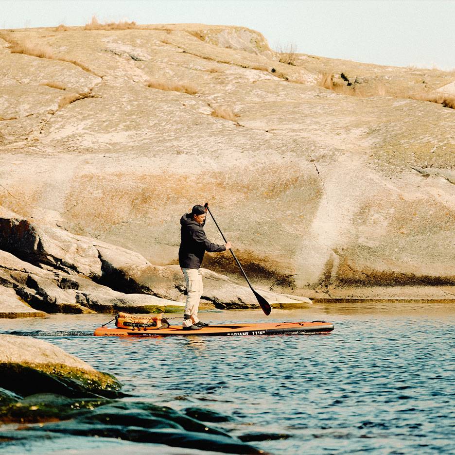 Man peddelt op een oranje stand-up paddleboard op een rotsachtig meer.