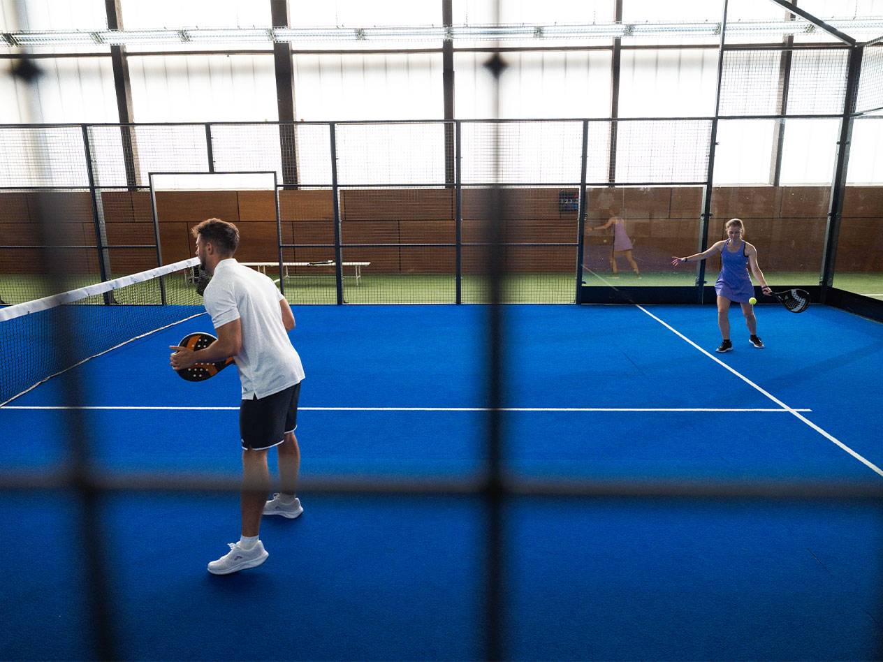 Man en vrouw spelen padel op een blauwe baan met rackets en bal.