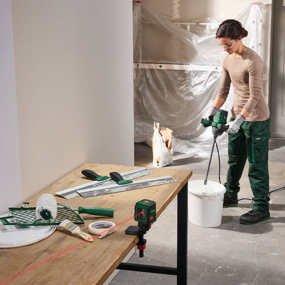 Vrouw mengt bouwmateriaal met schilder- en nivelleergereedschap op een tafel.