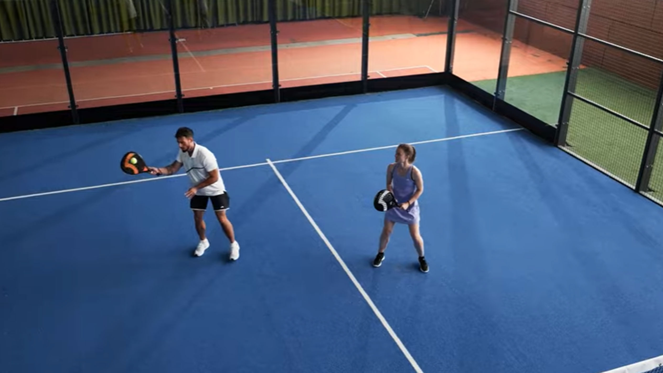Man en vrouw spelen padel op blauwe baan met rackets en bal