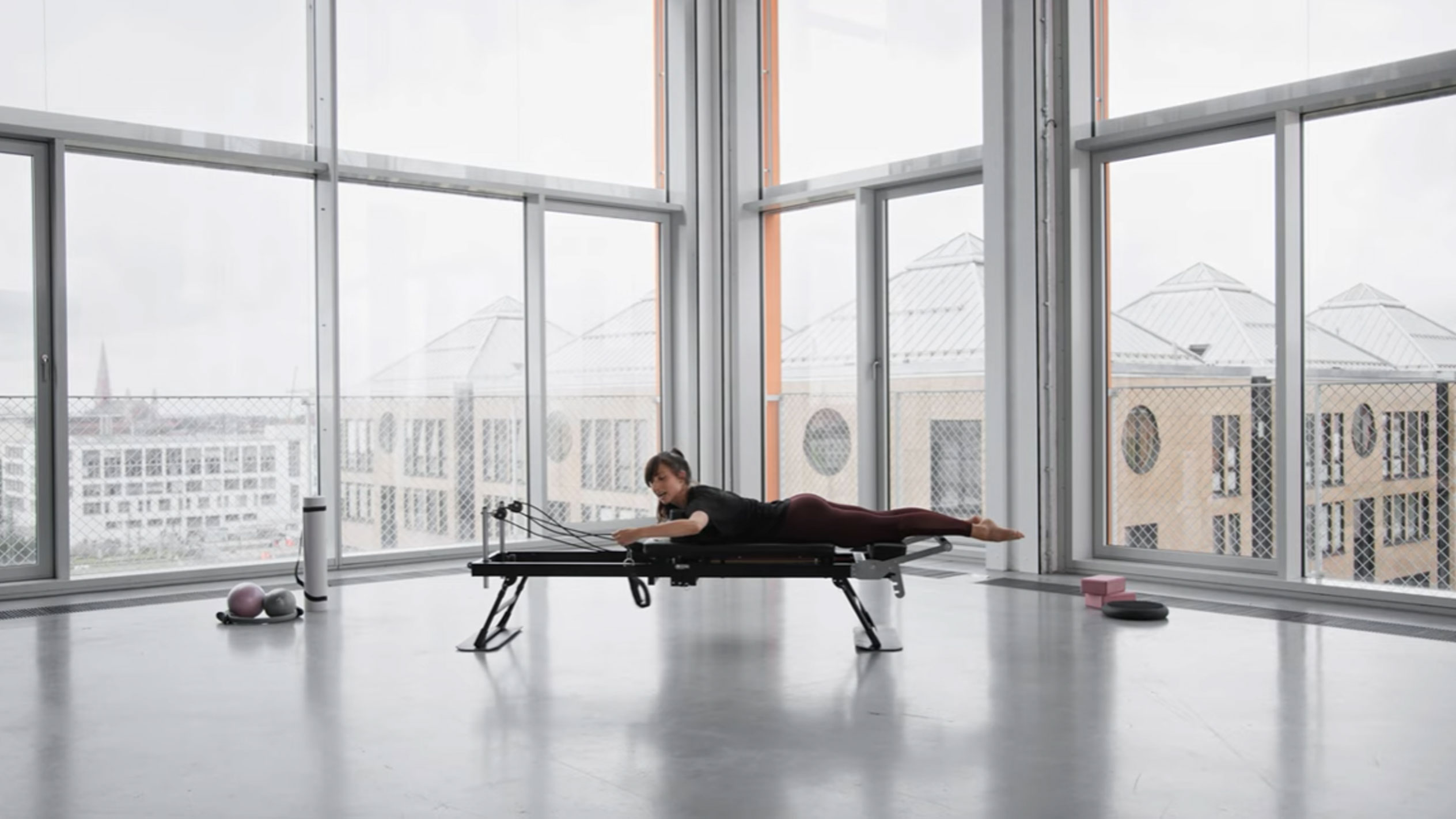 Vrouw doet Pilates op een reformer, met uitzicht op de stad.