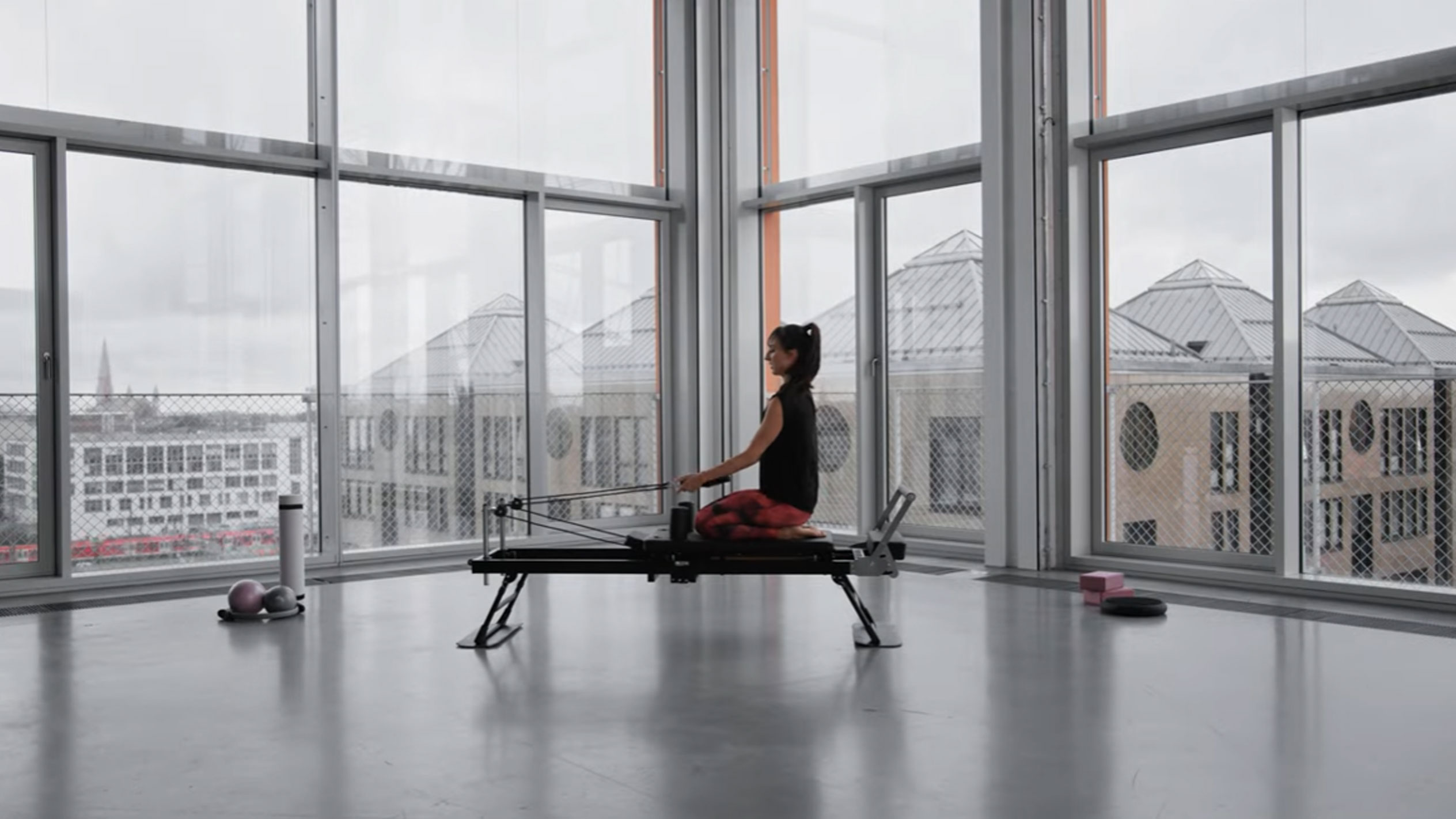 Vrouw doet Pilates op een reformer, met uitzicht op de stad.
