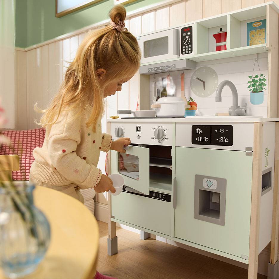 Kind speelt met een houten speelgoedkeuken, met oven, magnetron en koelkast.