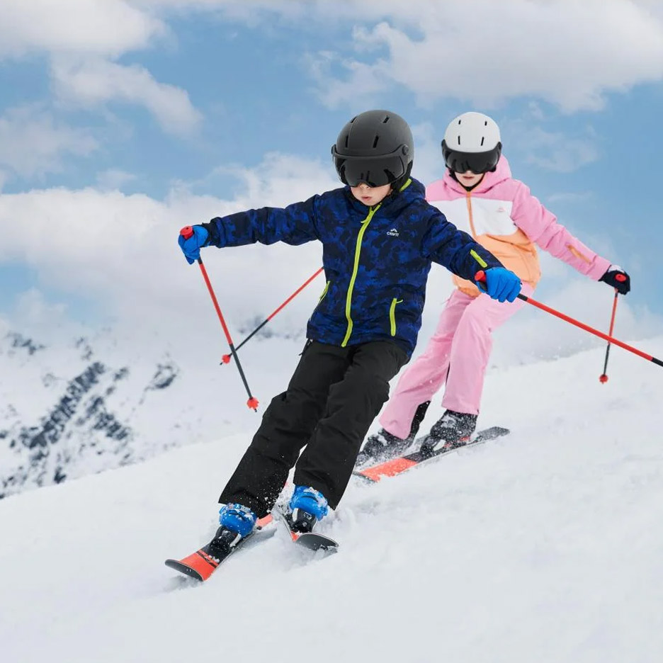 Twee kinderen skiën in Crivit ski-jassen, broeken en helmen op een besneeuwde berg.