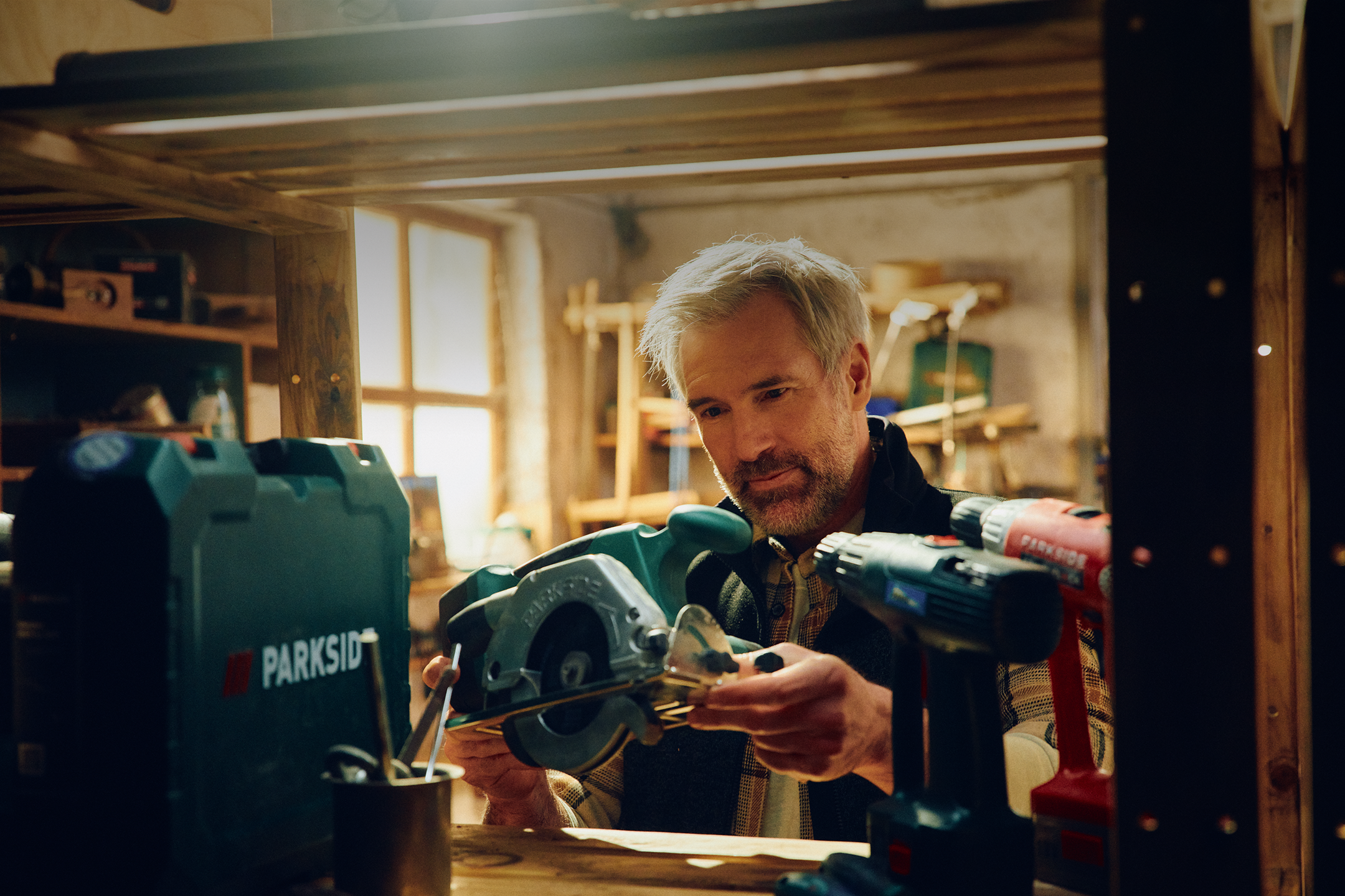 Een man onderzoekt een cirkelzaag in een werkplaats, met elektrisch gereedschap ernaast.