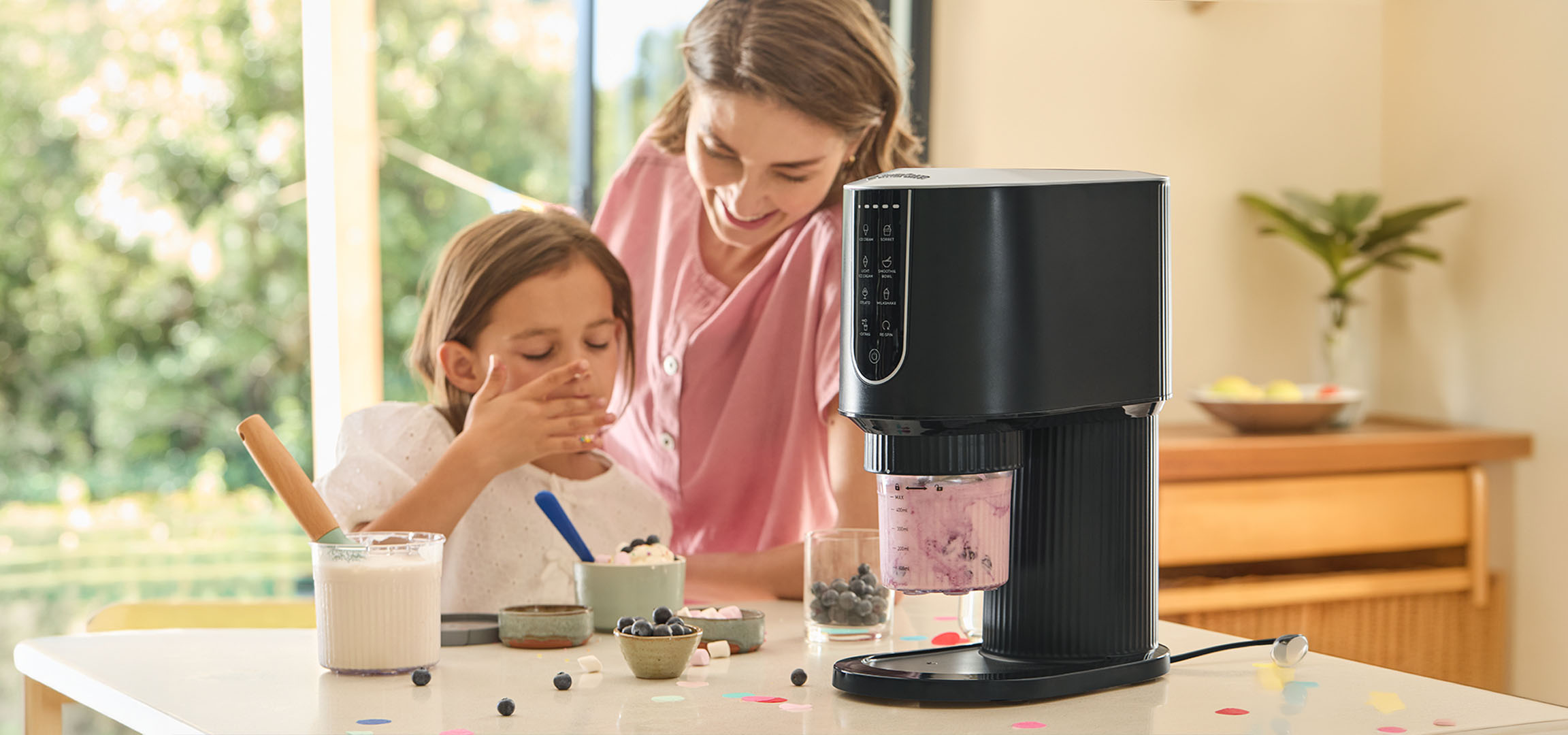 Vrouw en meisje maken desserts met een ijsmachine, omringd door bosbessen.
