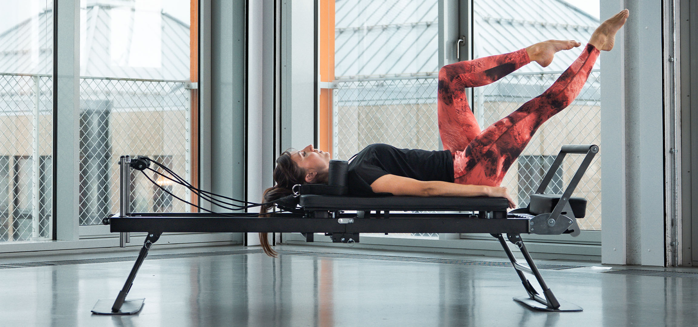 Vrouw doet Pilates op een reformer, met fitnessaccessoires in de buurt.