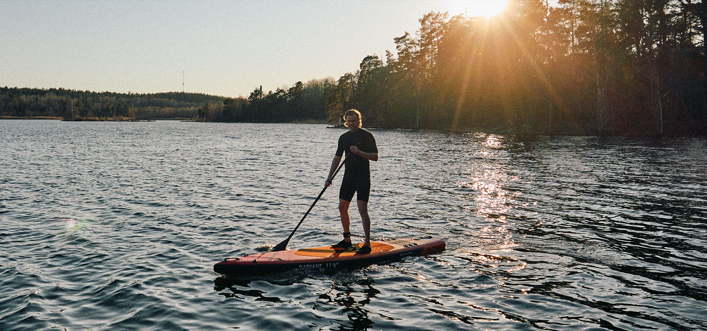Man op een stand-up paddleboard op een meer bij zonsondergang.