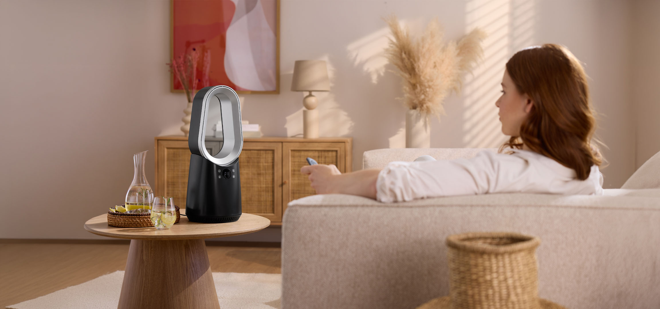 Vrouw op bank met afstandsbediening, moderne ventilator en drankjes op tafel.