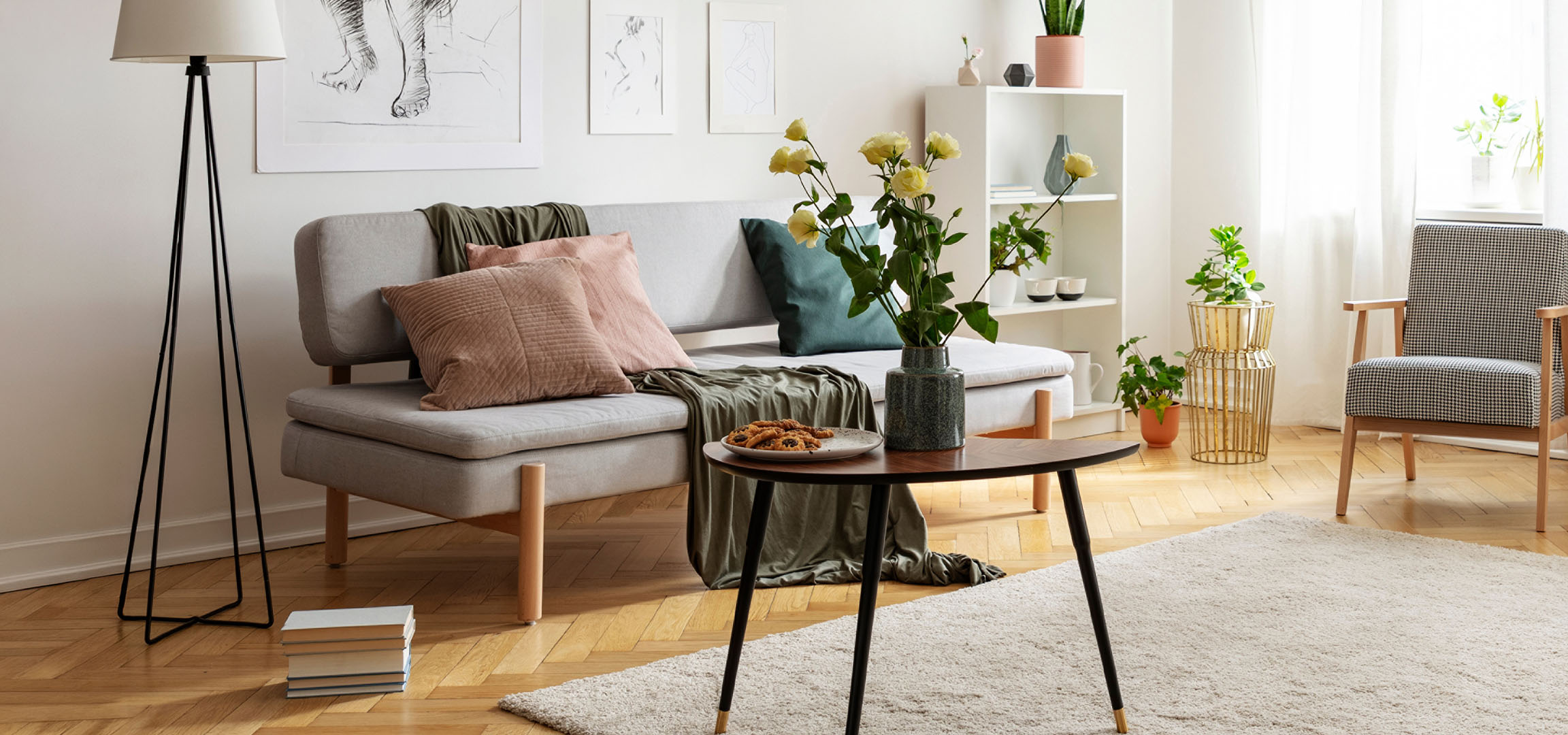 Gezellige woonkamer met een grijze bank, kussens, een salontafel met koekjes en een vaas met bloemen.