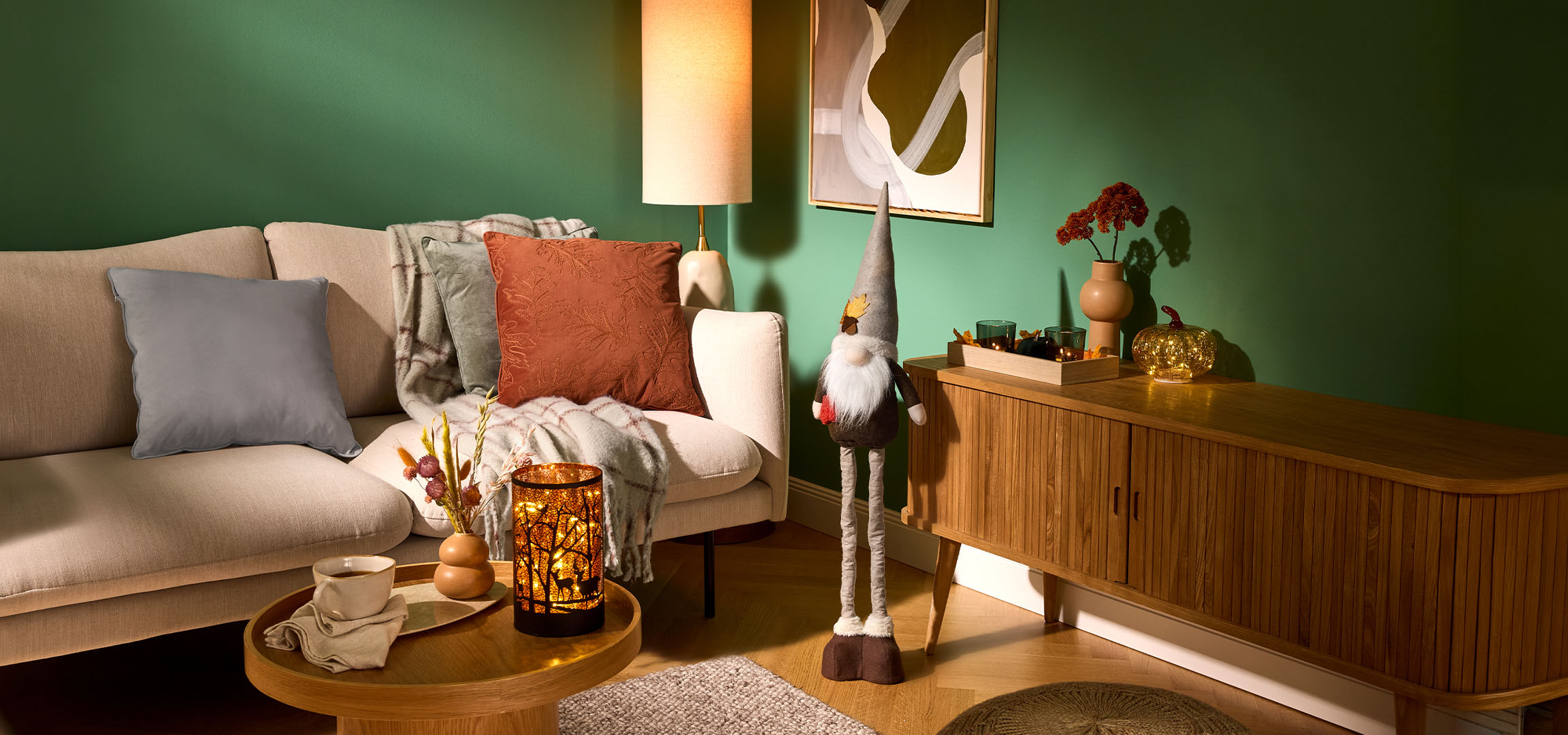 Gezellige woonkamer met beige bank, kussens, deken en herfstdecoraties.