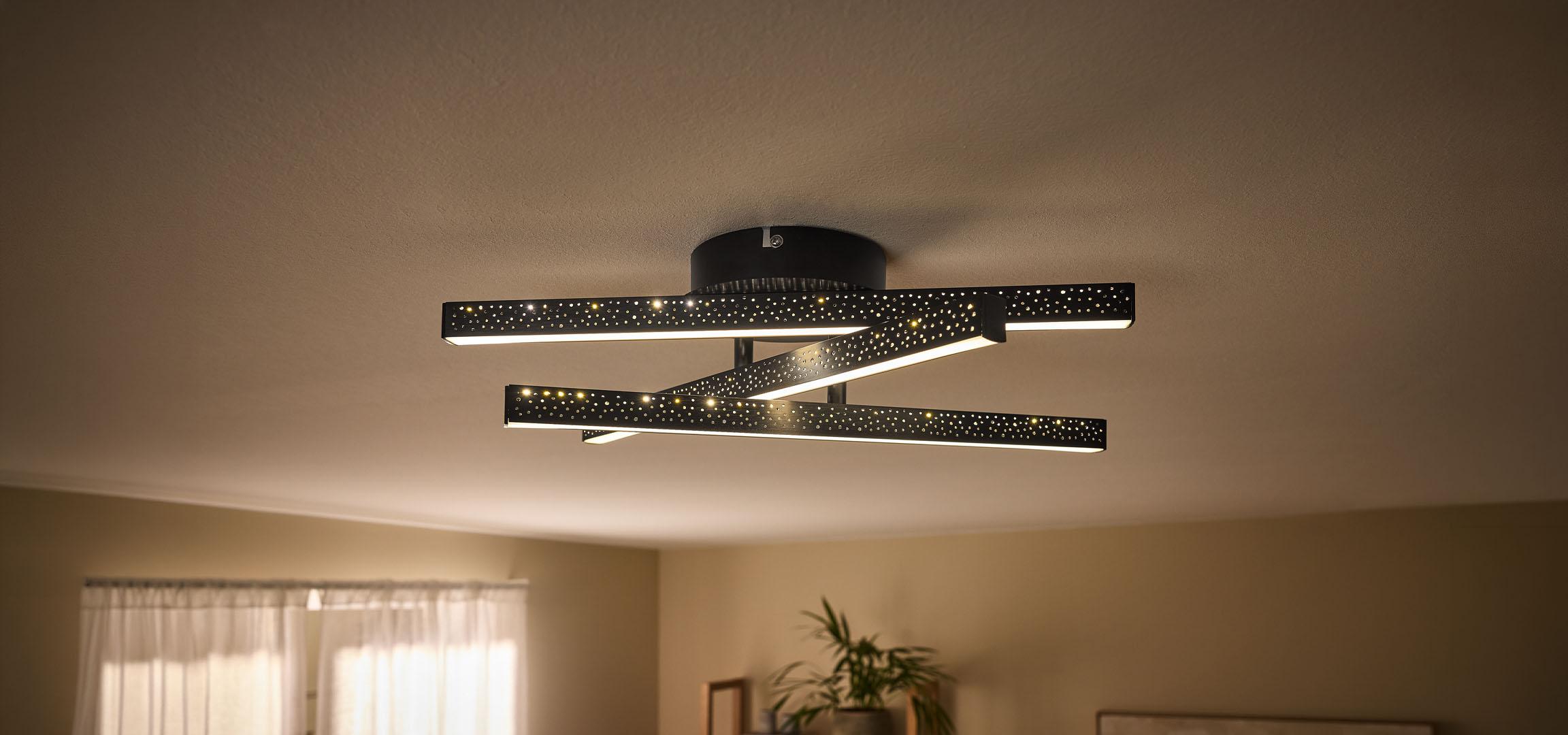 Moderne LED-plafondlamp met zwarte, geperforeerde stangen en warm licht.
