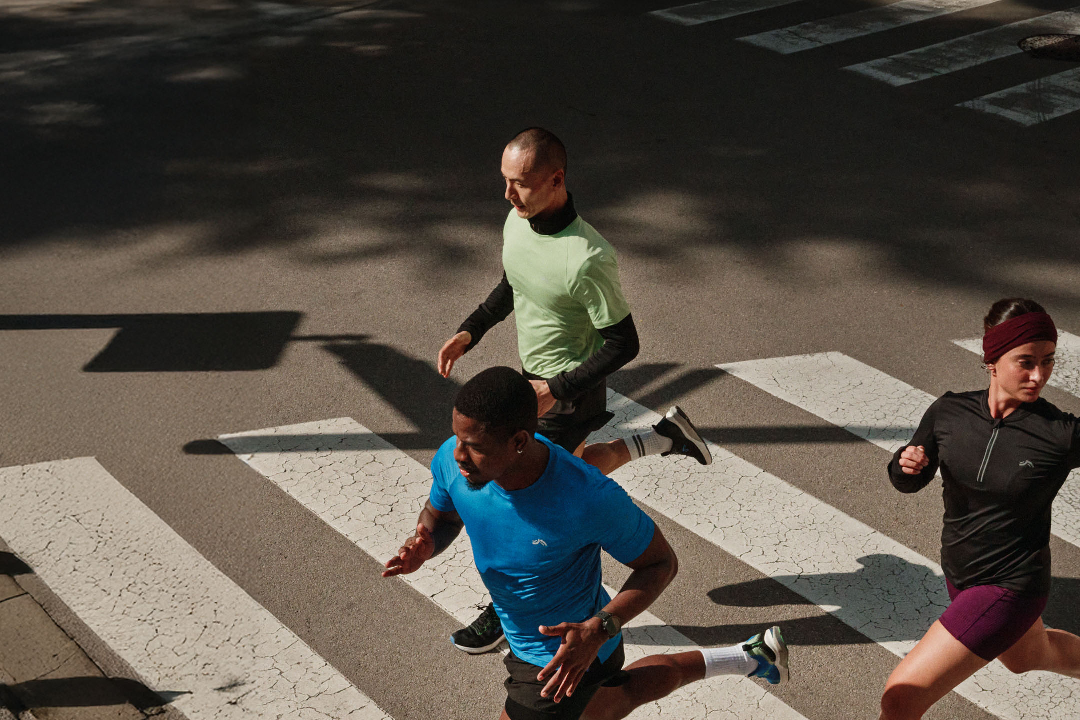 Drie hardlopers in sportkleding steken een zebrapad over in de stad.