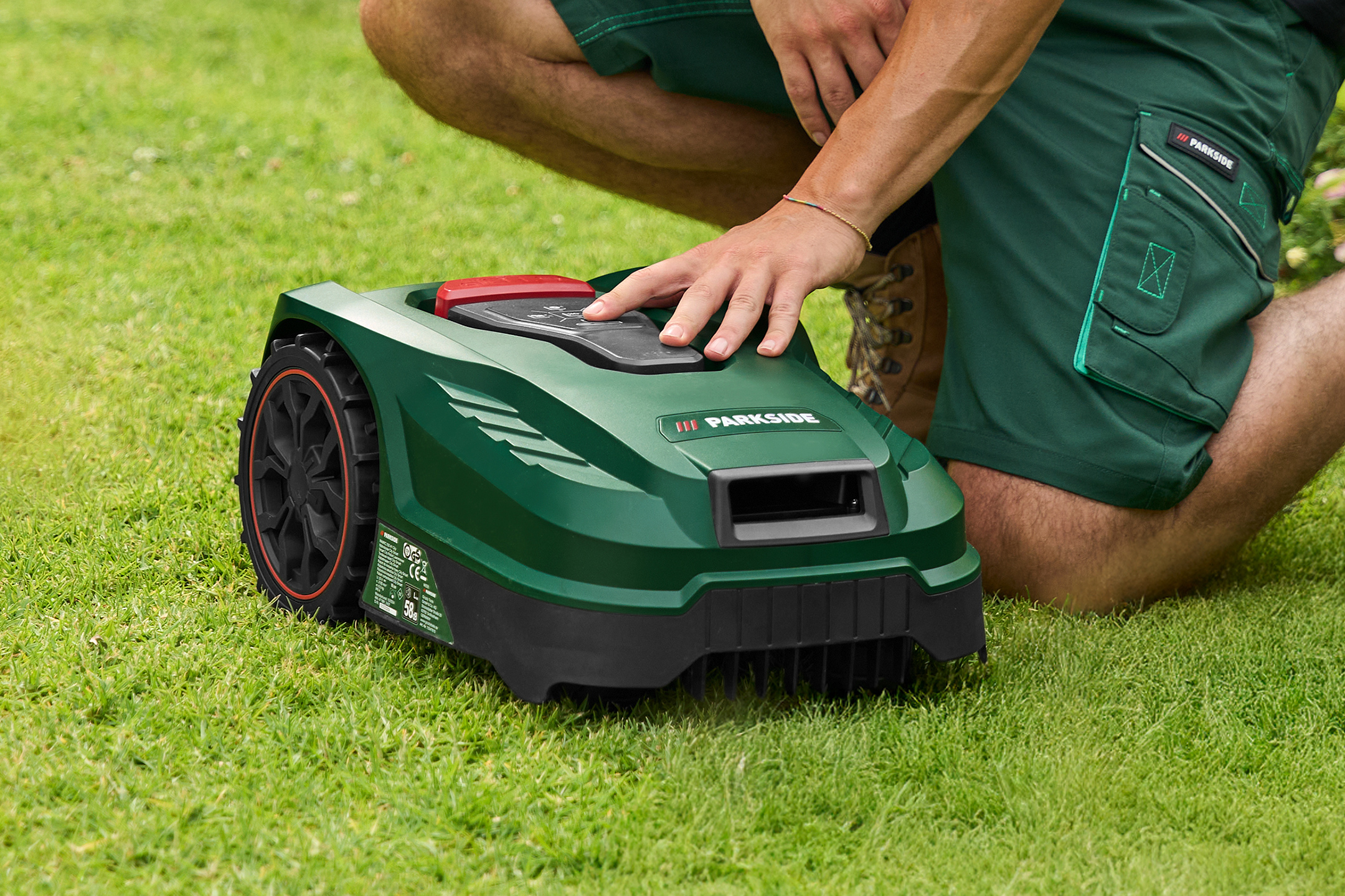 Man knielt en bedient een groene robotmaaier op een gazon.