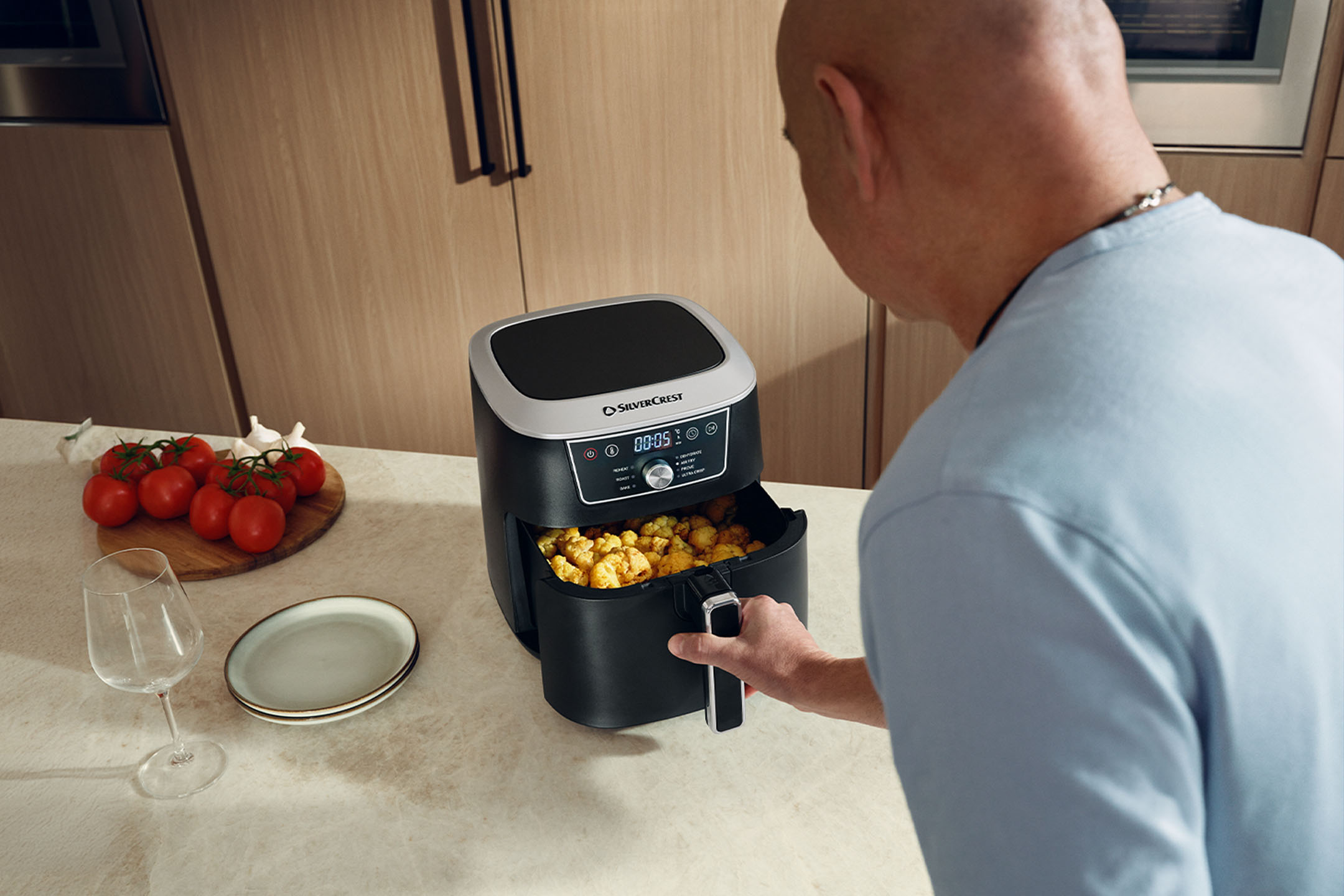 Man kookt met een airfryer in de keuken, met tomaten en borden.