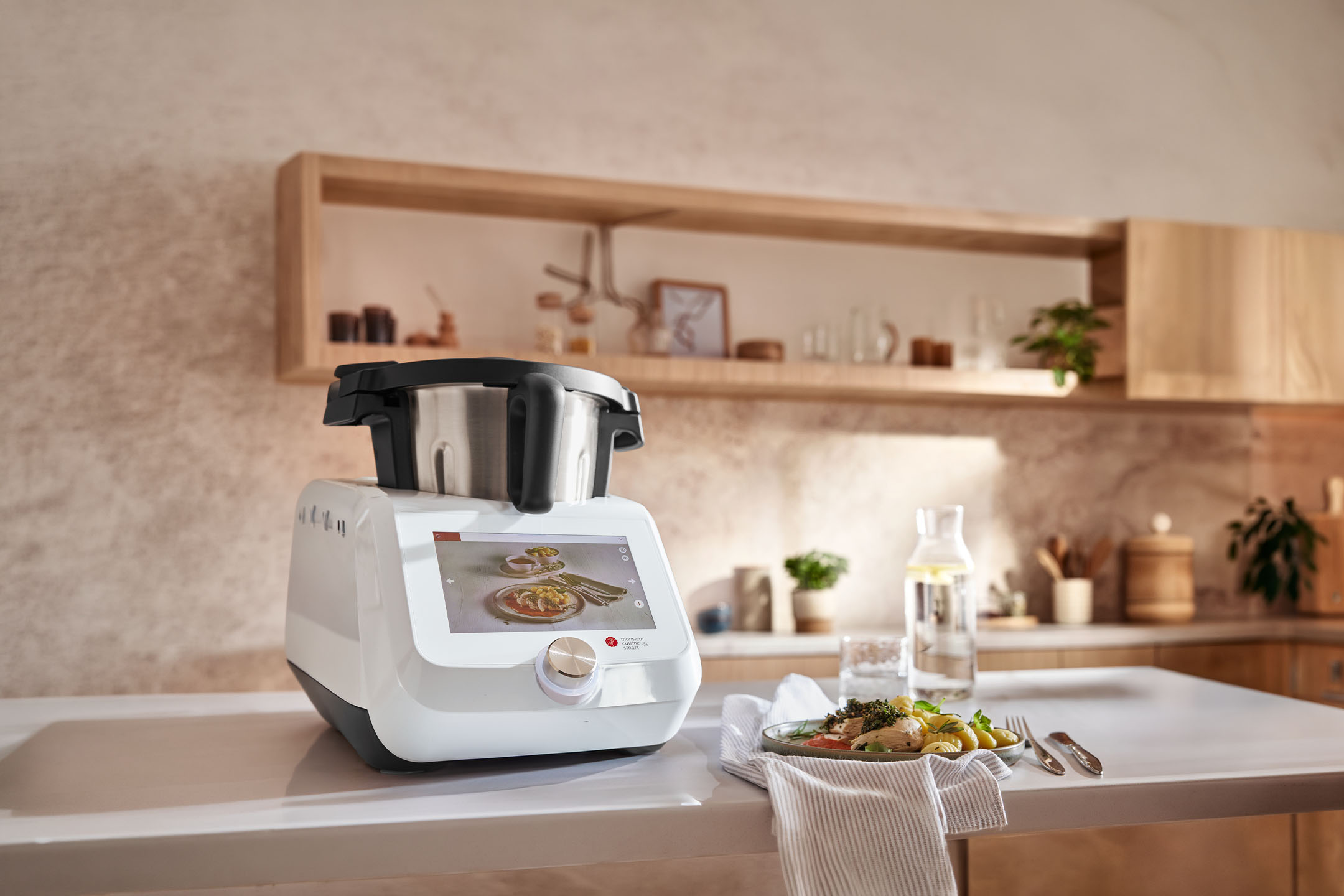 Slim keukenapparaat op een aanrecht met een bereide maaltijd en waterfles in een moderne keuken.