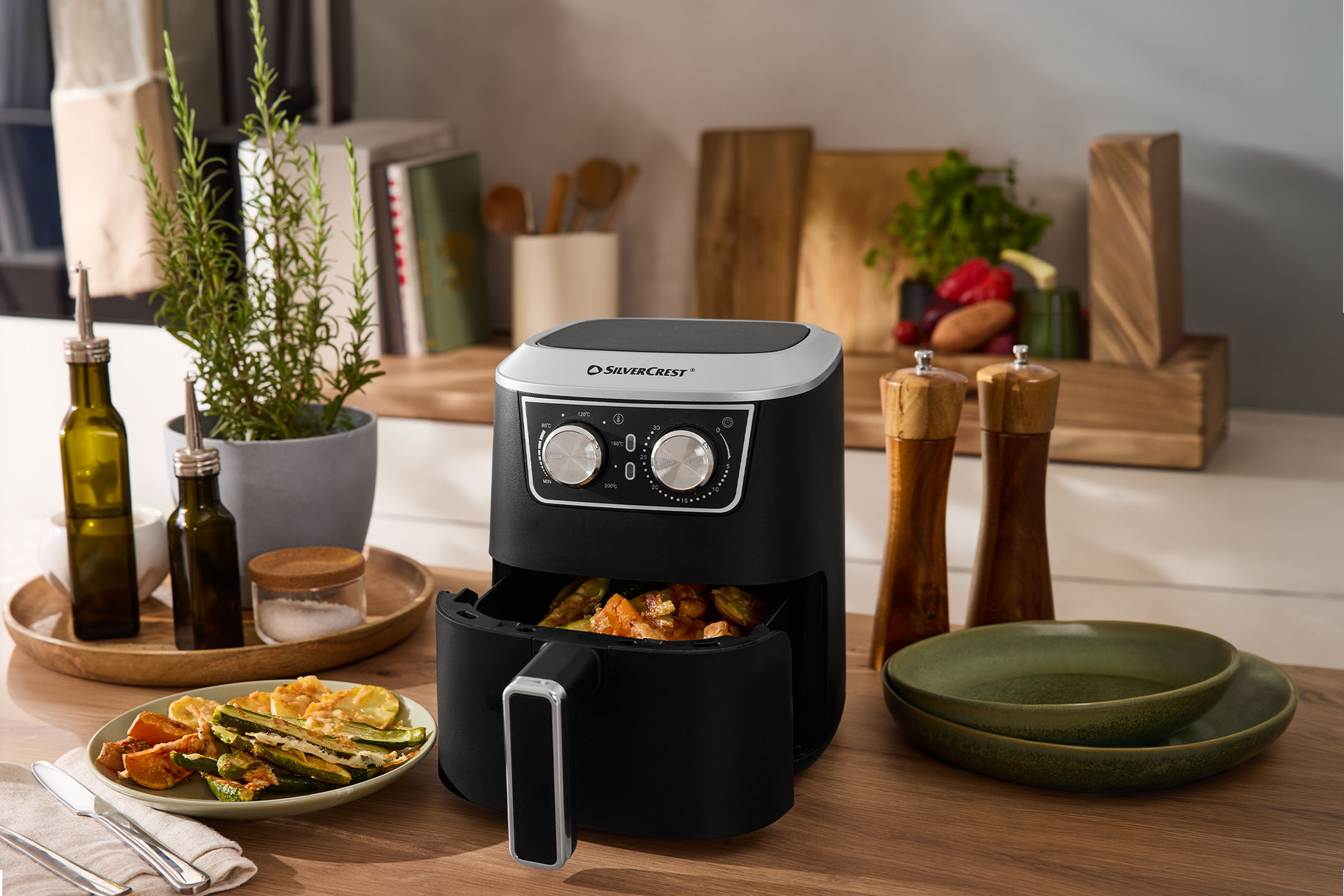 Zwarte airfryer met geroosterde groenten, kruiden en specerijen in een keuken.