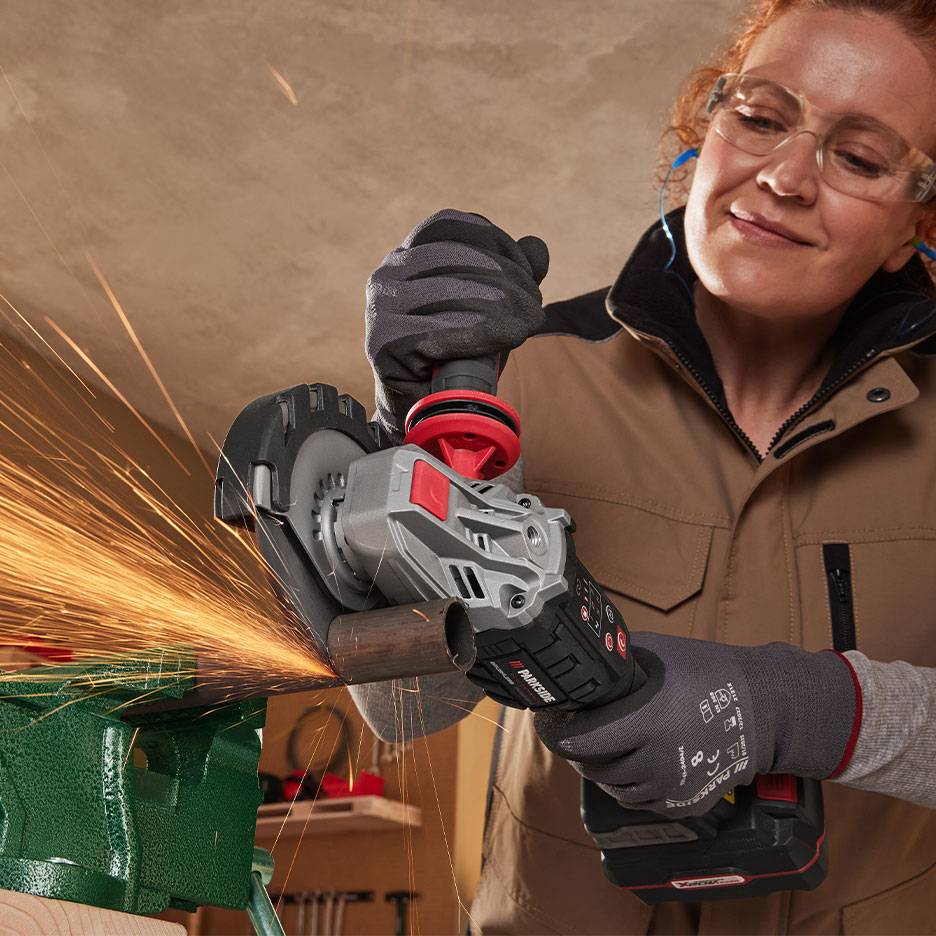 Vrouw met veiligheidsbril gebruikt een draadloze haakse slijper om een metalen pijp te snijden.