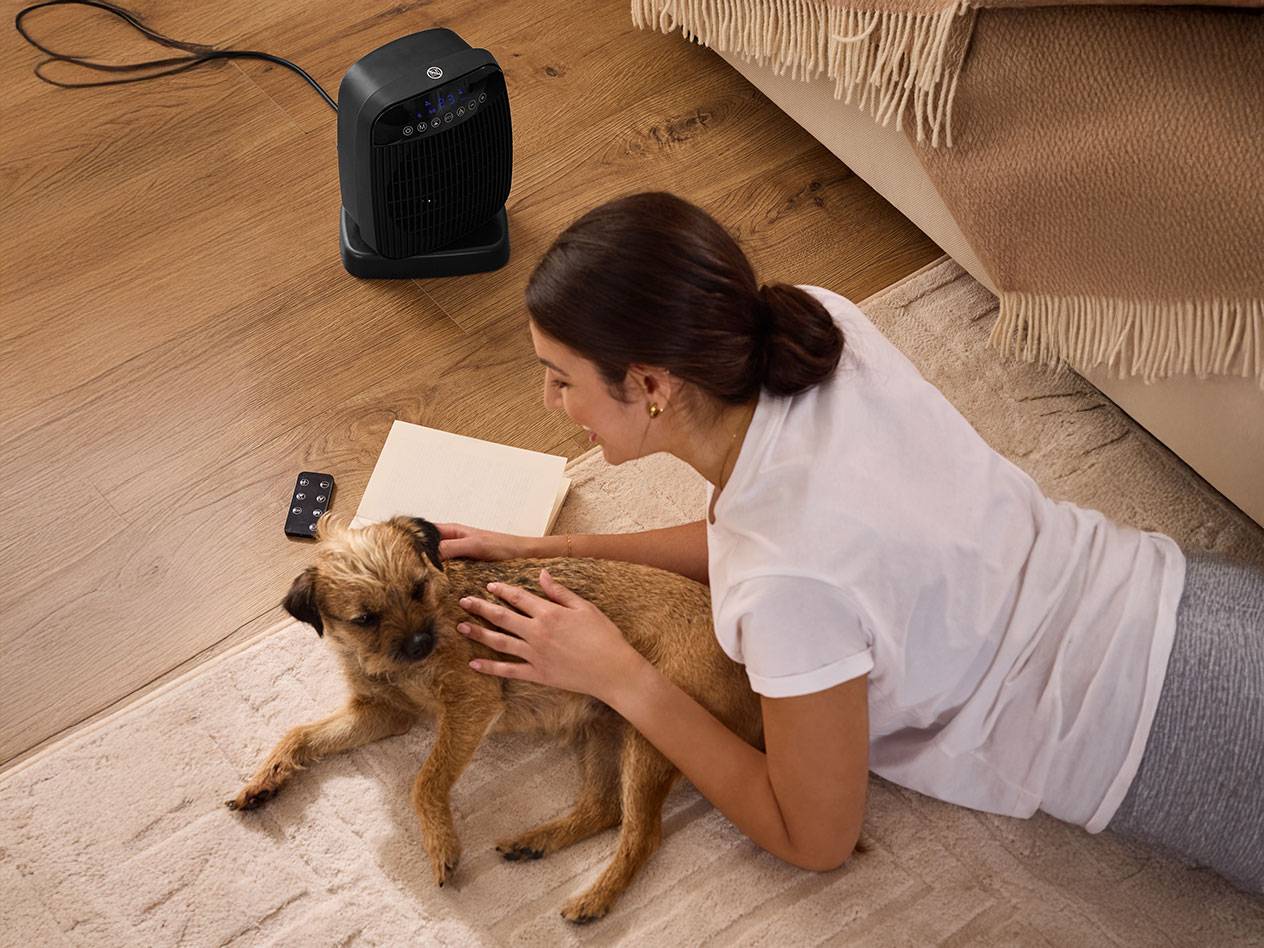 Vrouw aait hond naast zwarte ruimteverwarmer op de vloer.