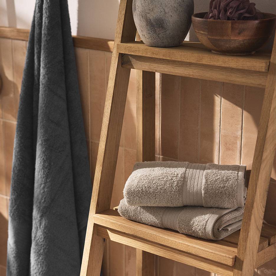 Grijze handdoeken op een houten plank en ladder in een betegelde badkamer.