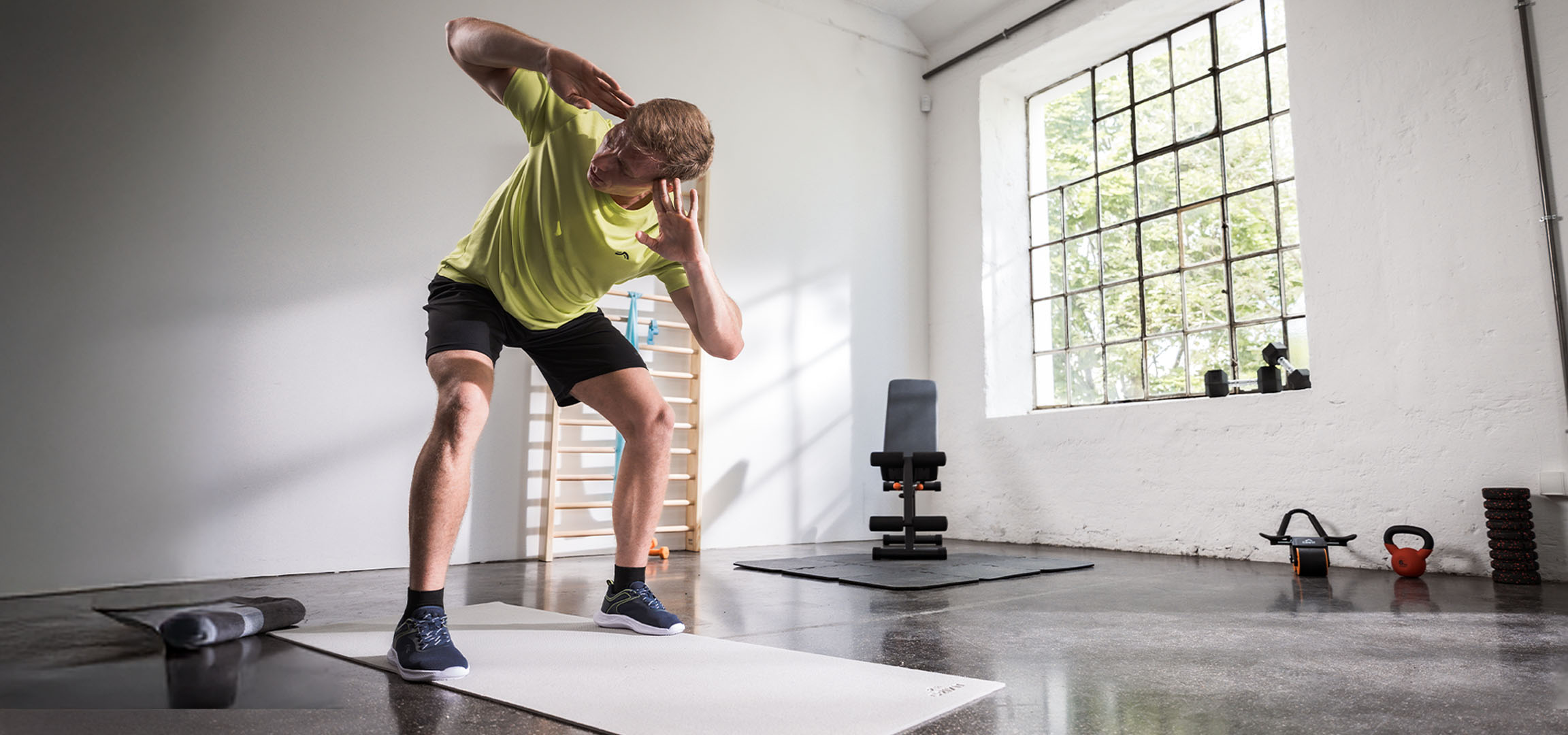 Man die traint in een sportschool, met een yogamat en dumbbells.