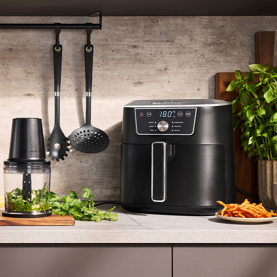 SilverCrest airfryer en hakmolen op een aanrecht met verse kruiden en zoete aardappelfrietjes.