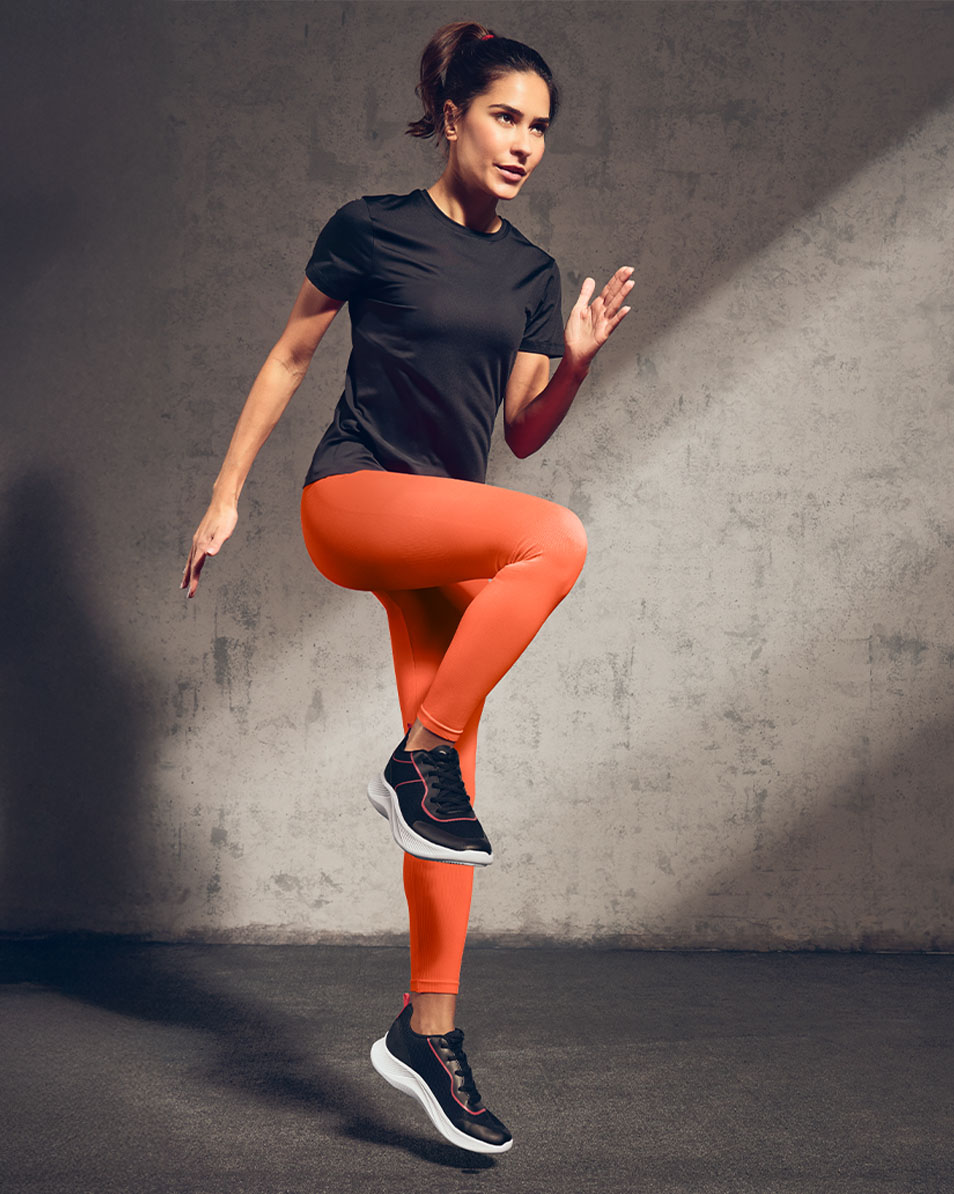 Vrouw in zwart sportshirt en oranje legging aan het sporten