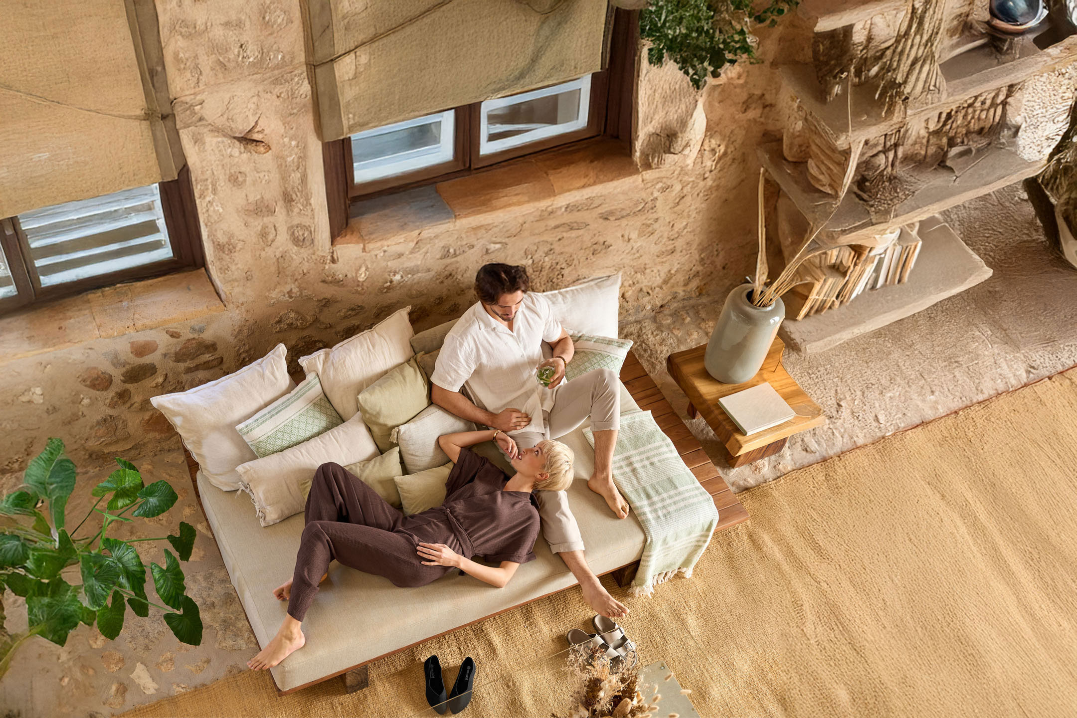 Paar ontspant op een bank met kussens en plaids, in een gezellig, rustiek interieur.