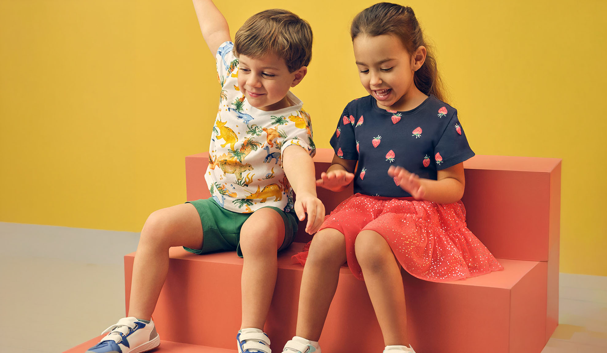 Twee kinderen in zomerkleding, een jongen in een dinosaurus T-shirt en een meisje in een aardbeien T-shirt.