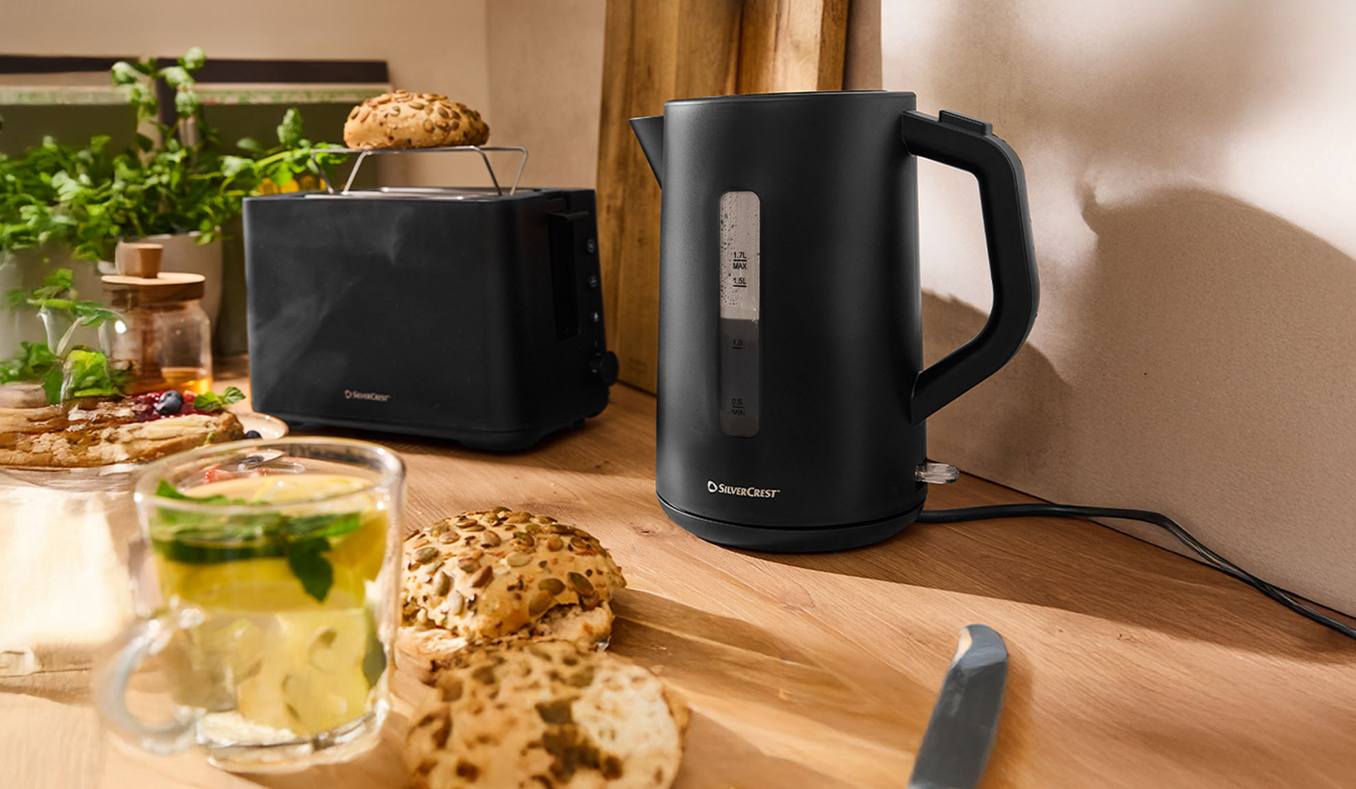 Zwarte SilverCrest waterkoker en broodrooster op een houten tafel met ontbijt.