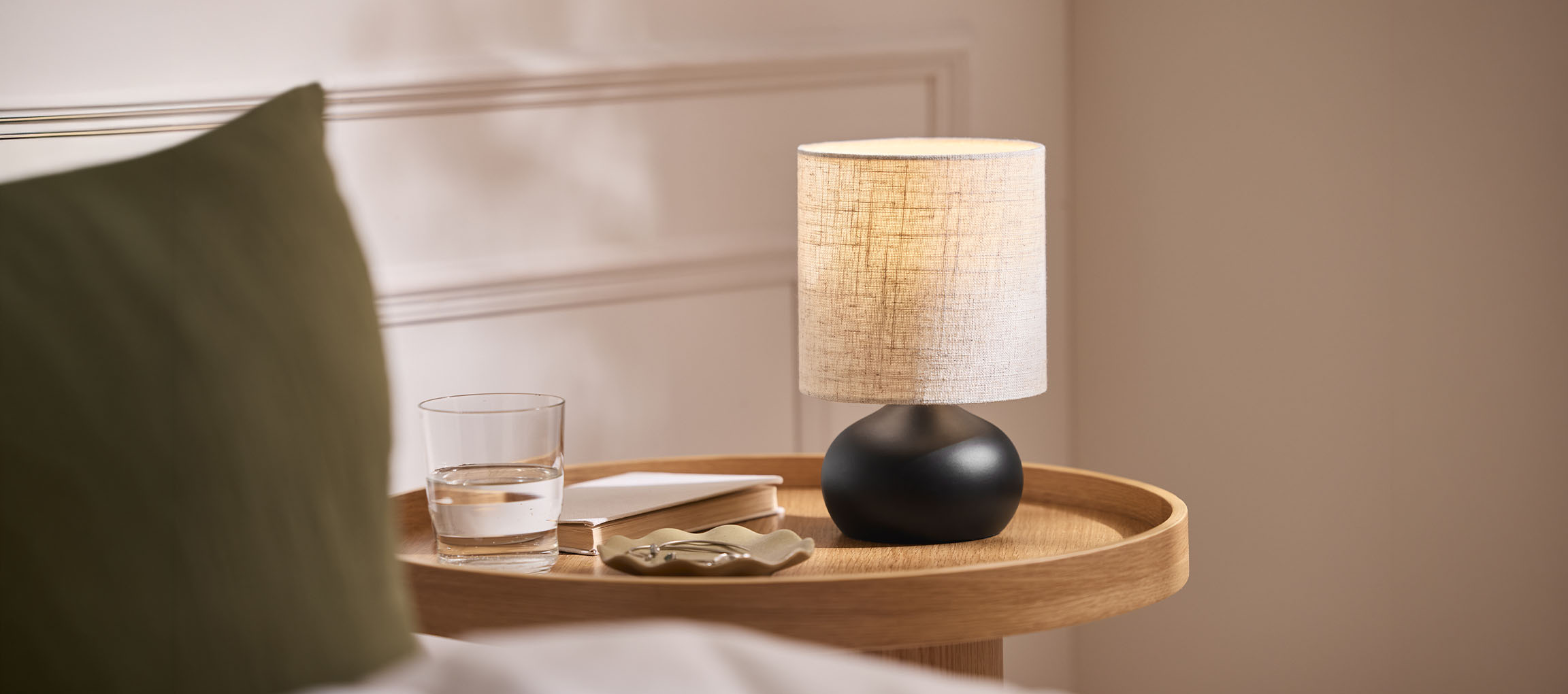 Bedlampje met stoffen kap, glas water en boek op een houten dienblad.