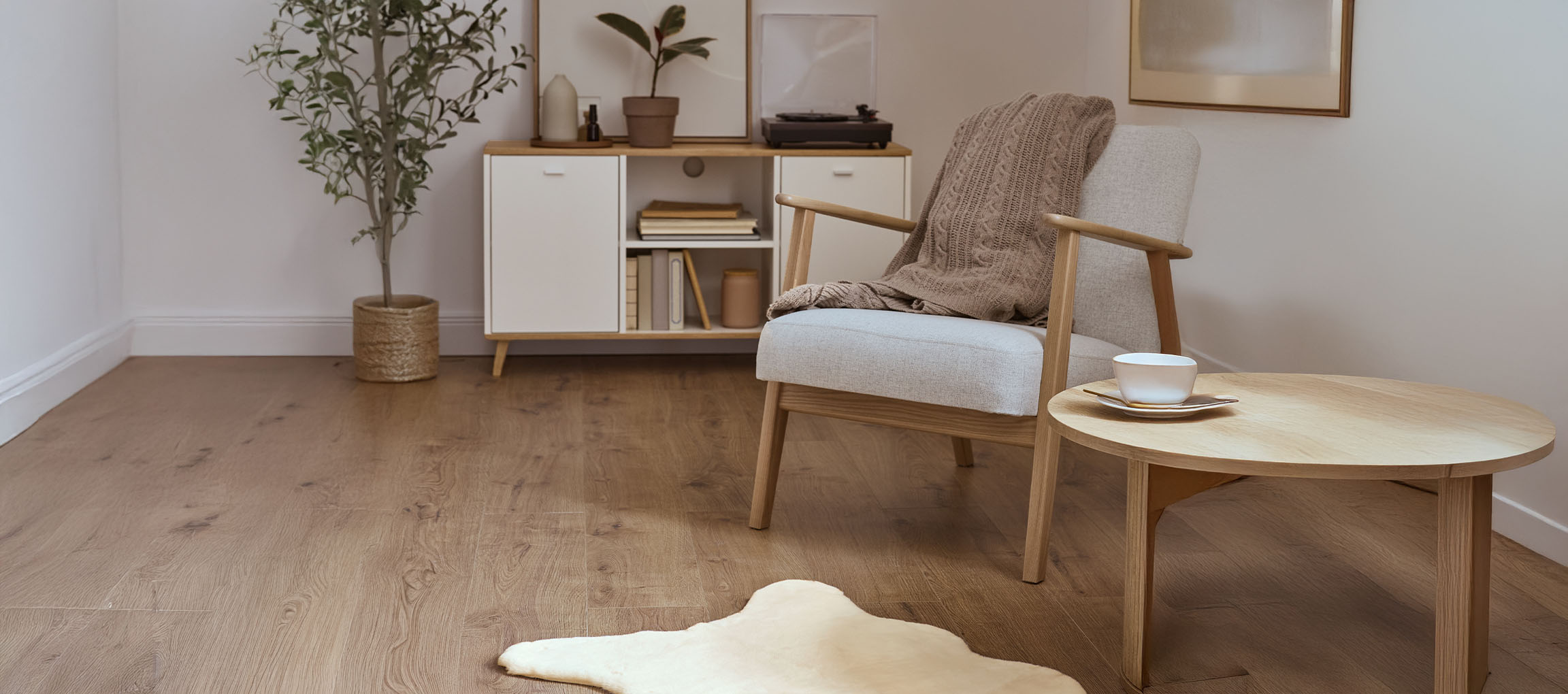 Grijze stoffen fauteuil met gebreide plaid, houten salontafel en modern dressoir.