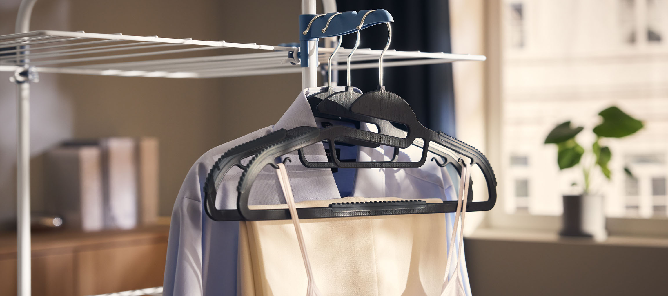 Kleding op hangers aan een droogrek, met een plant op de achtergrond.