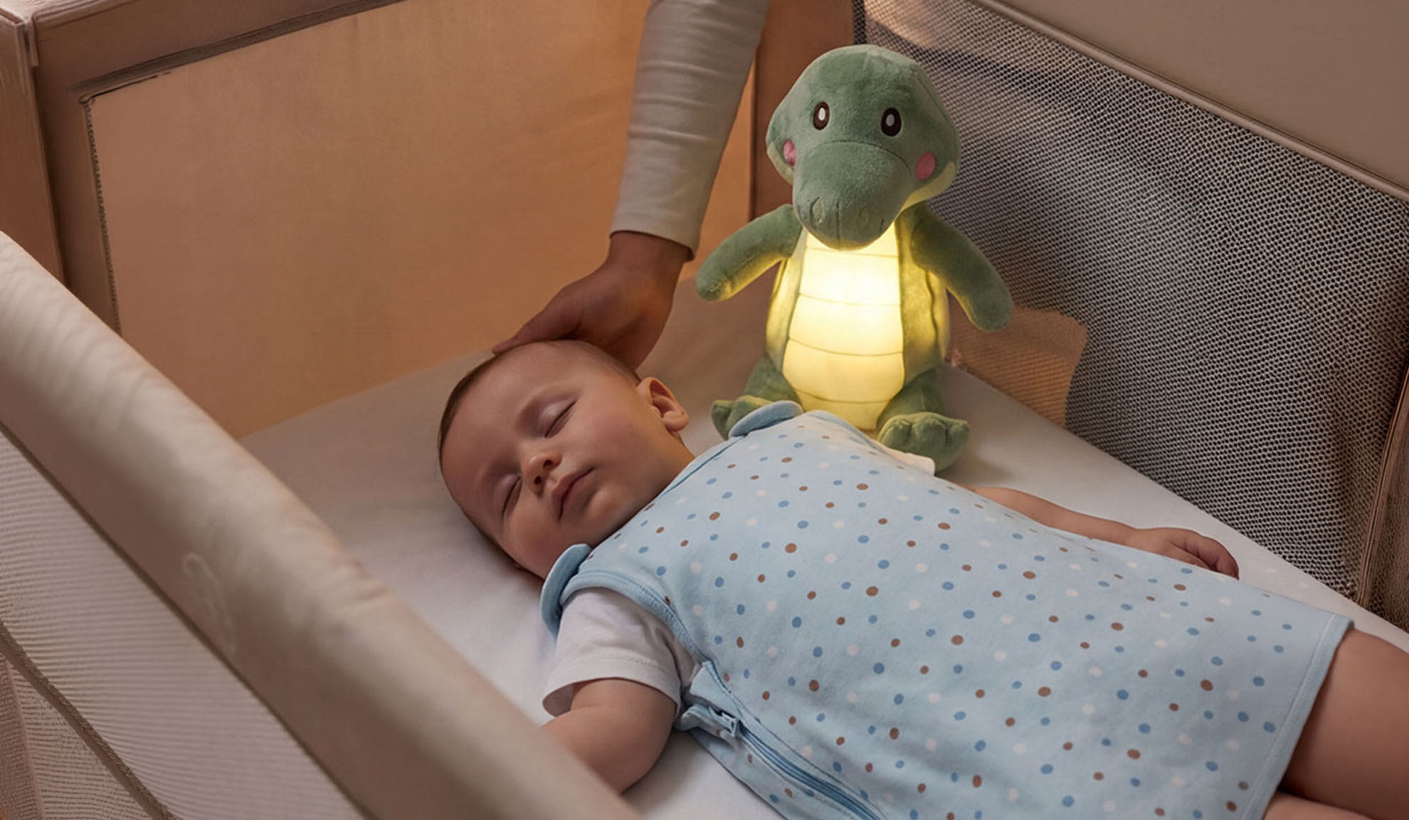 Baby slaapt in wieg met knuffel en hand van ouder.