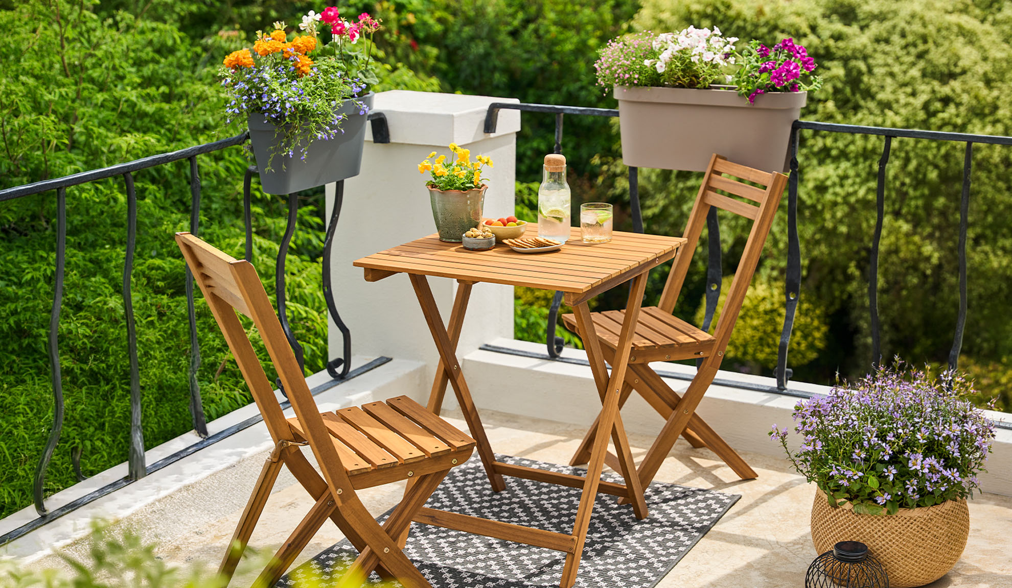Balkon met houten bistroset, potplanten en drankjes op een patroonkleed.