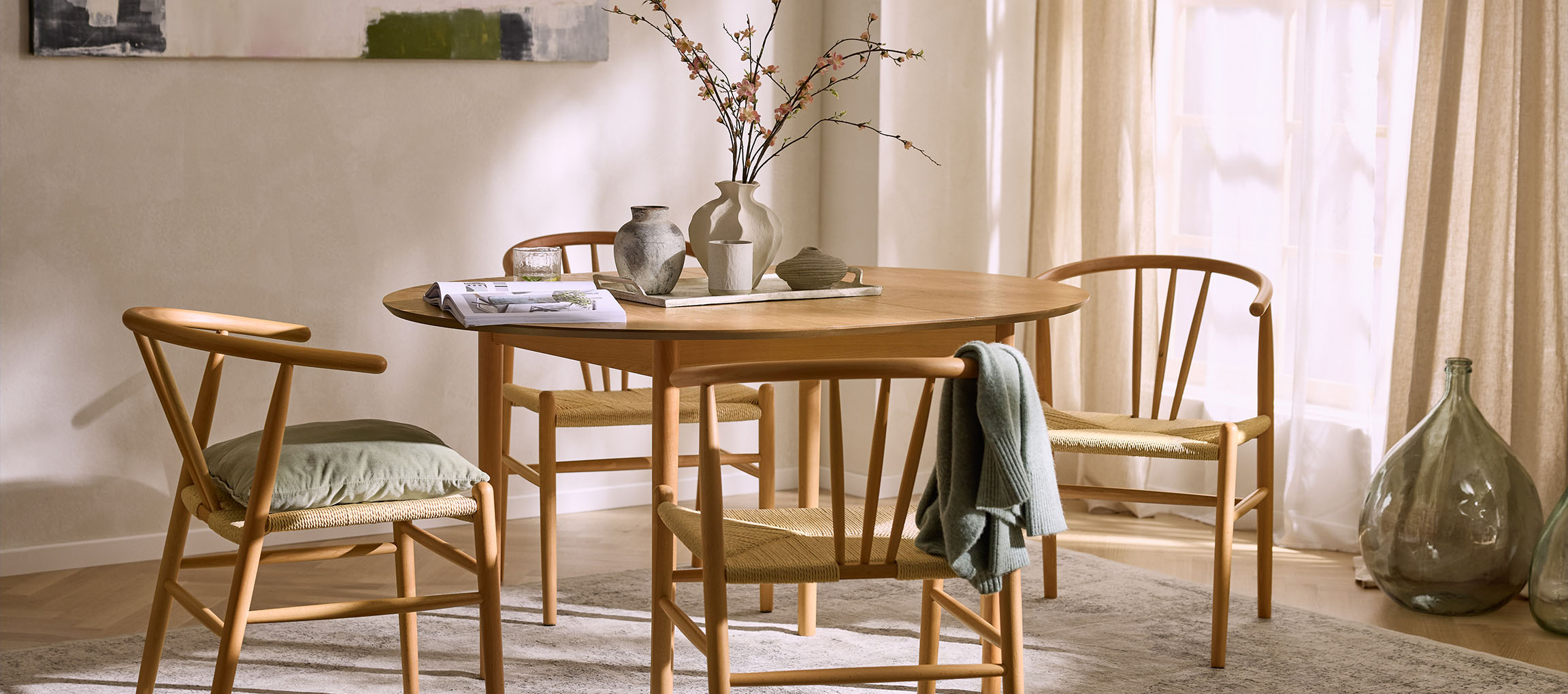 Eetkamer met een ronde houten tafel, houten stoelen met touwzittingen en decoratieve vazen.