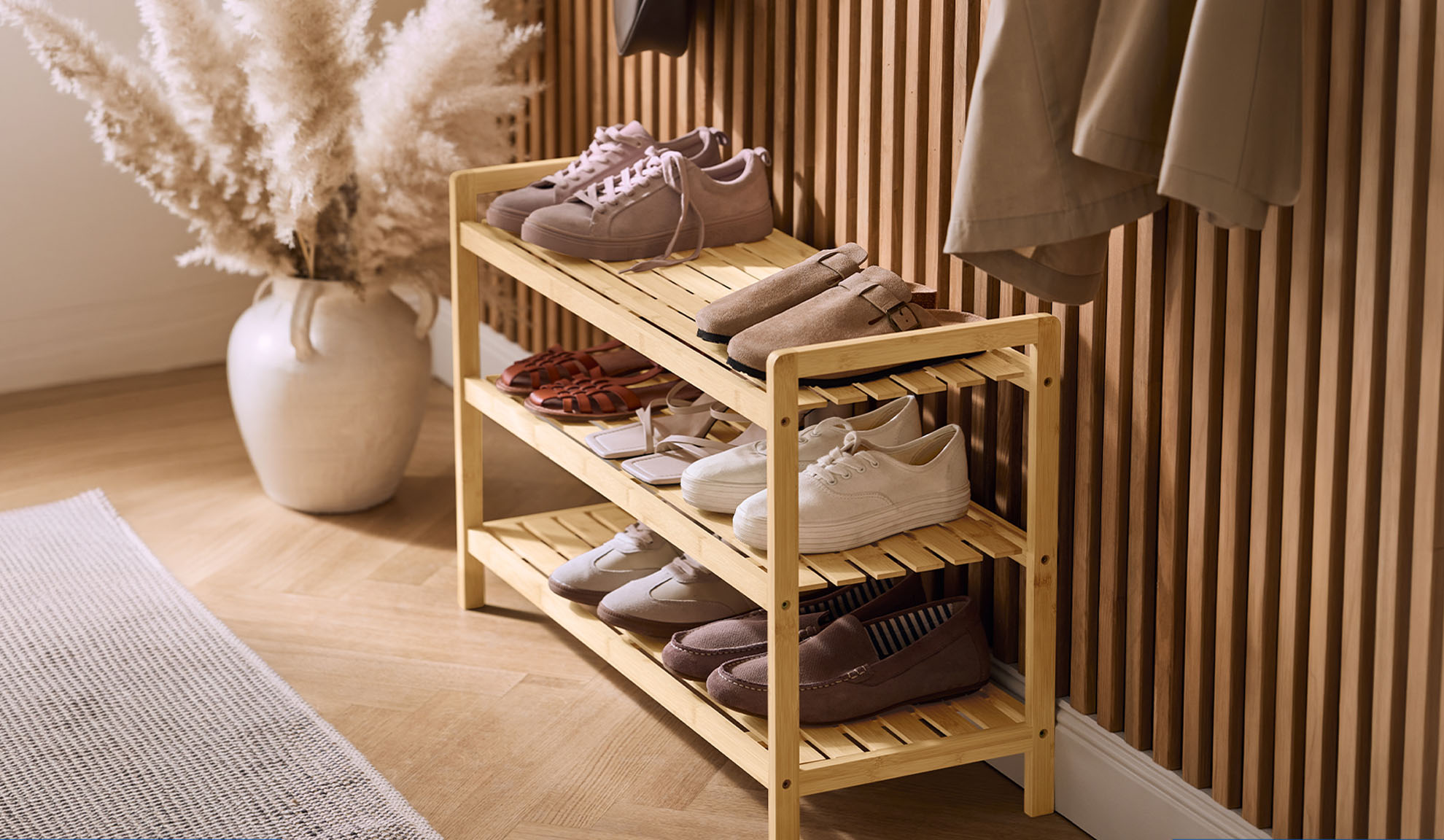 Houten schoenenrek met diverse schoenen en een vaas met pampasgras in de hal.