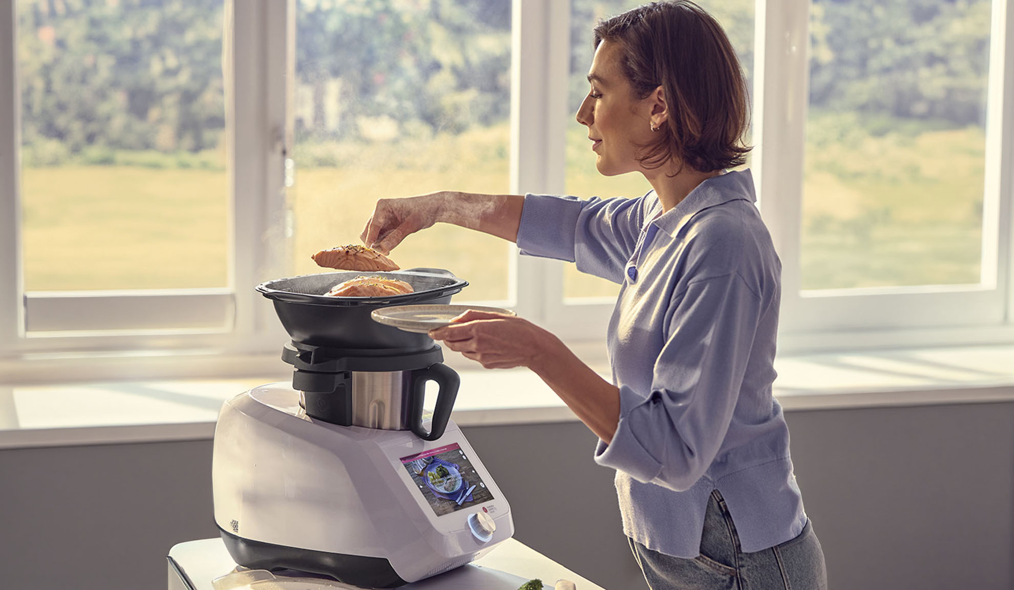 Vrouw bereidt zalm in een keukenmachine met stoomfunctie, met behulp van het digitale scherm.