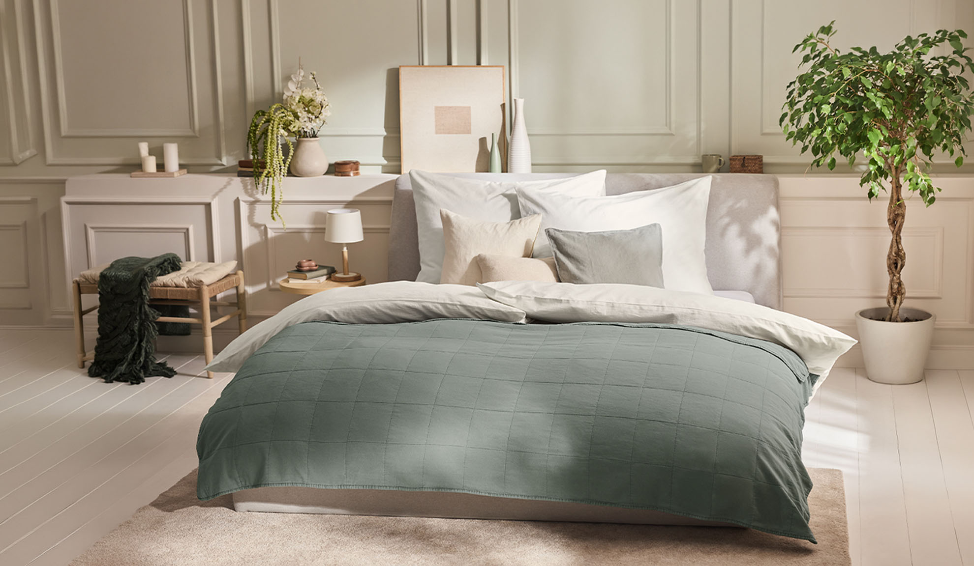 Slaapkamer met bed, groen dekbedovertrek, witte kussens en plant