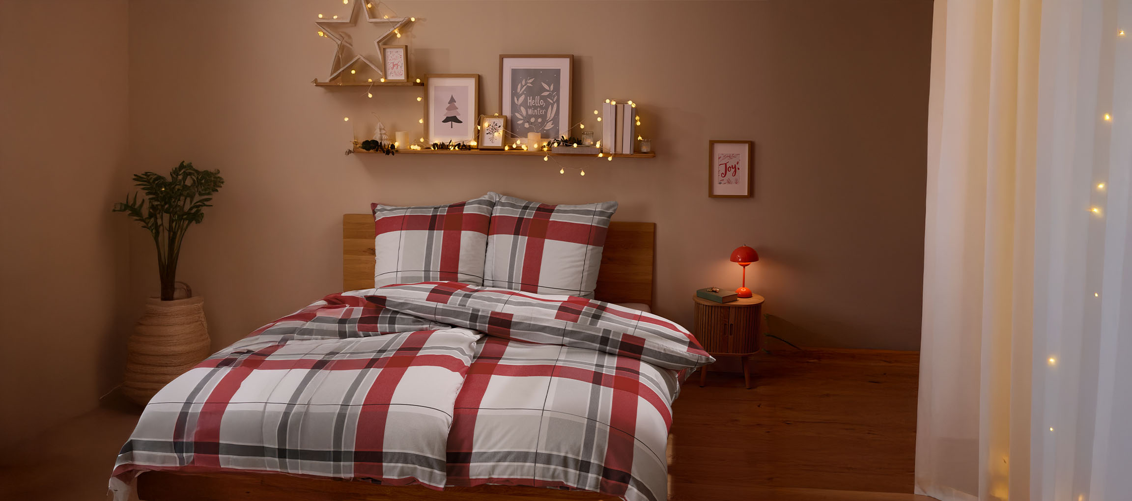 Gezellige slaapkamer met rood en grijs geruit beddengoed, kerstdecoratie en lichtslingers.
