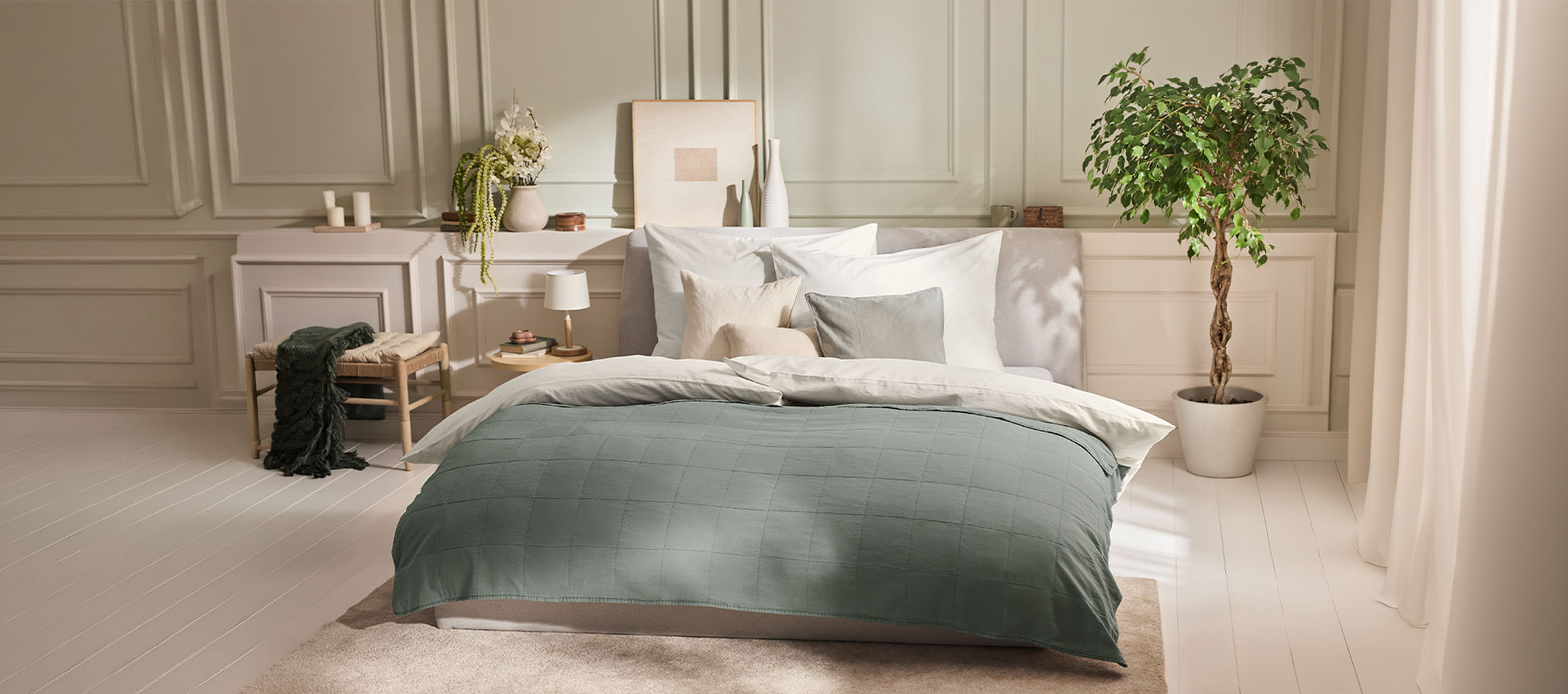 Slaapkamer met bed, groene sprei, kussens, nachtkastje en plant.