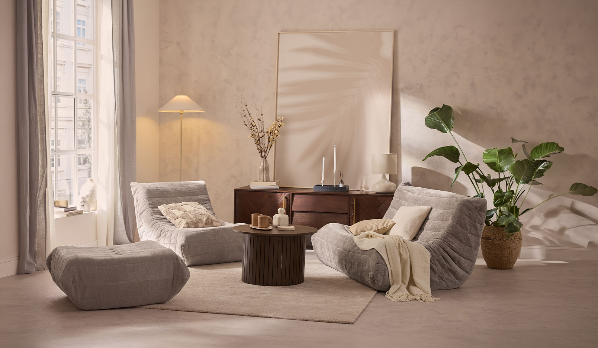 Gezellige woonkamer met twee grijze loungestoelen, poef, salontafel en plant.