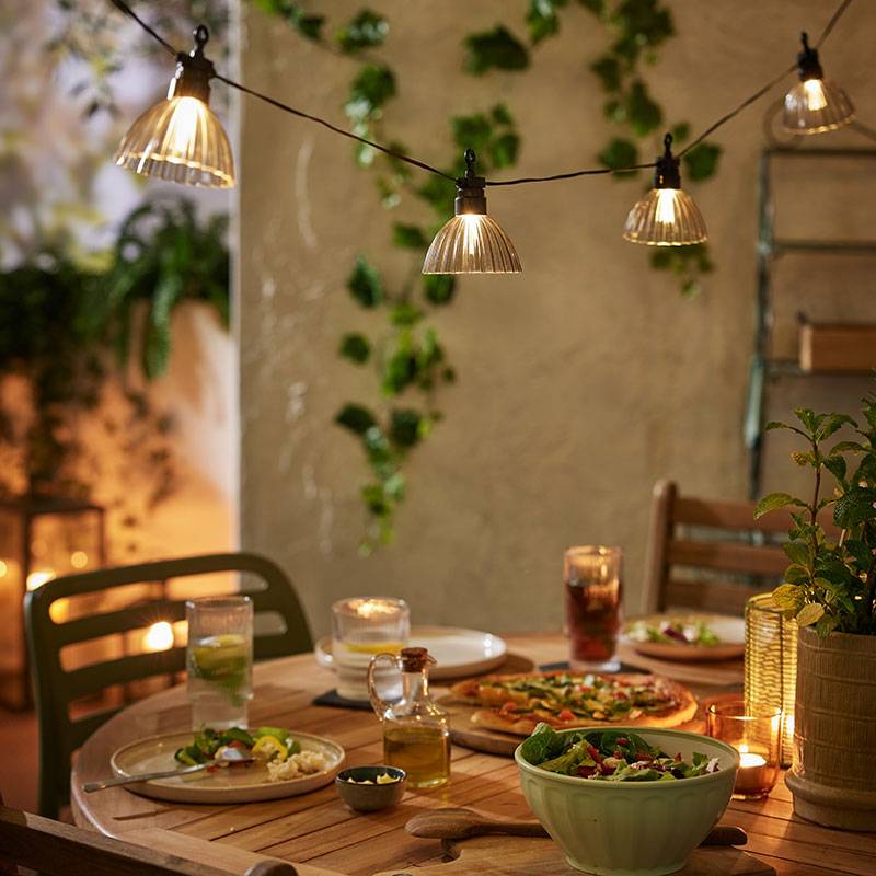 Buitenverlichting met warme lampjes boven een houten tafel met eten.