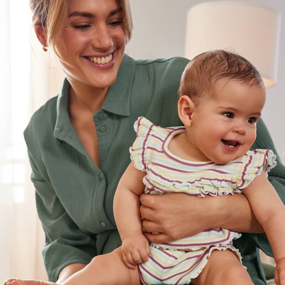 Lachende moeder met blije baby in een kleurrijke gestreepte outfit.