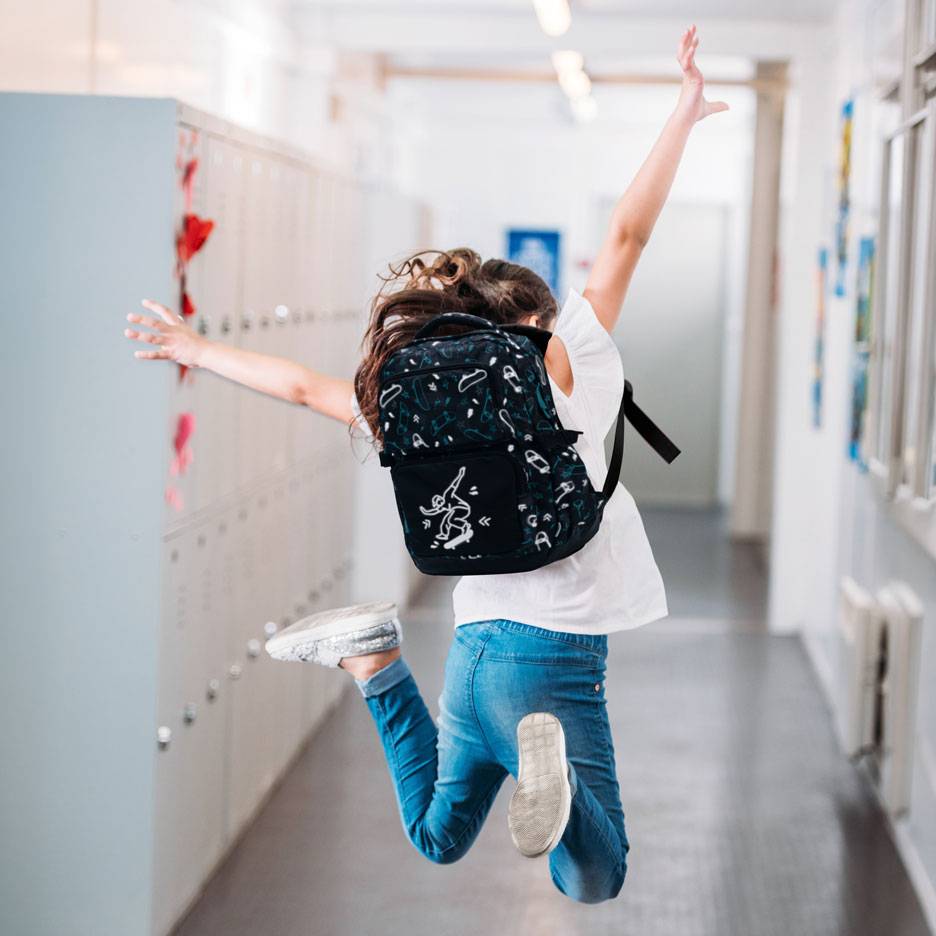 Kind met rugzak springt in een schoolgang.