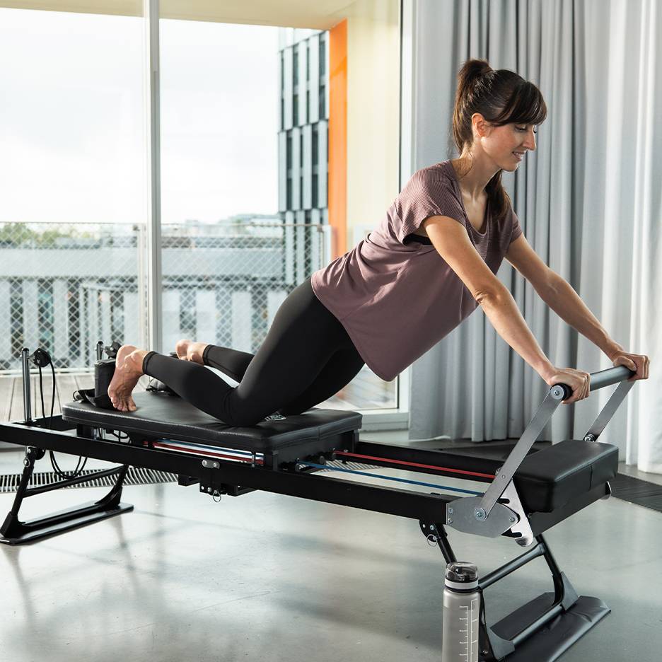 Vrouw doet Pilates op een reformer met veren en banden.